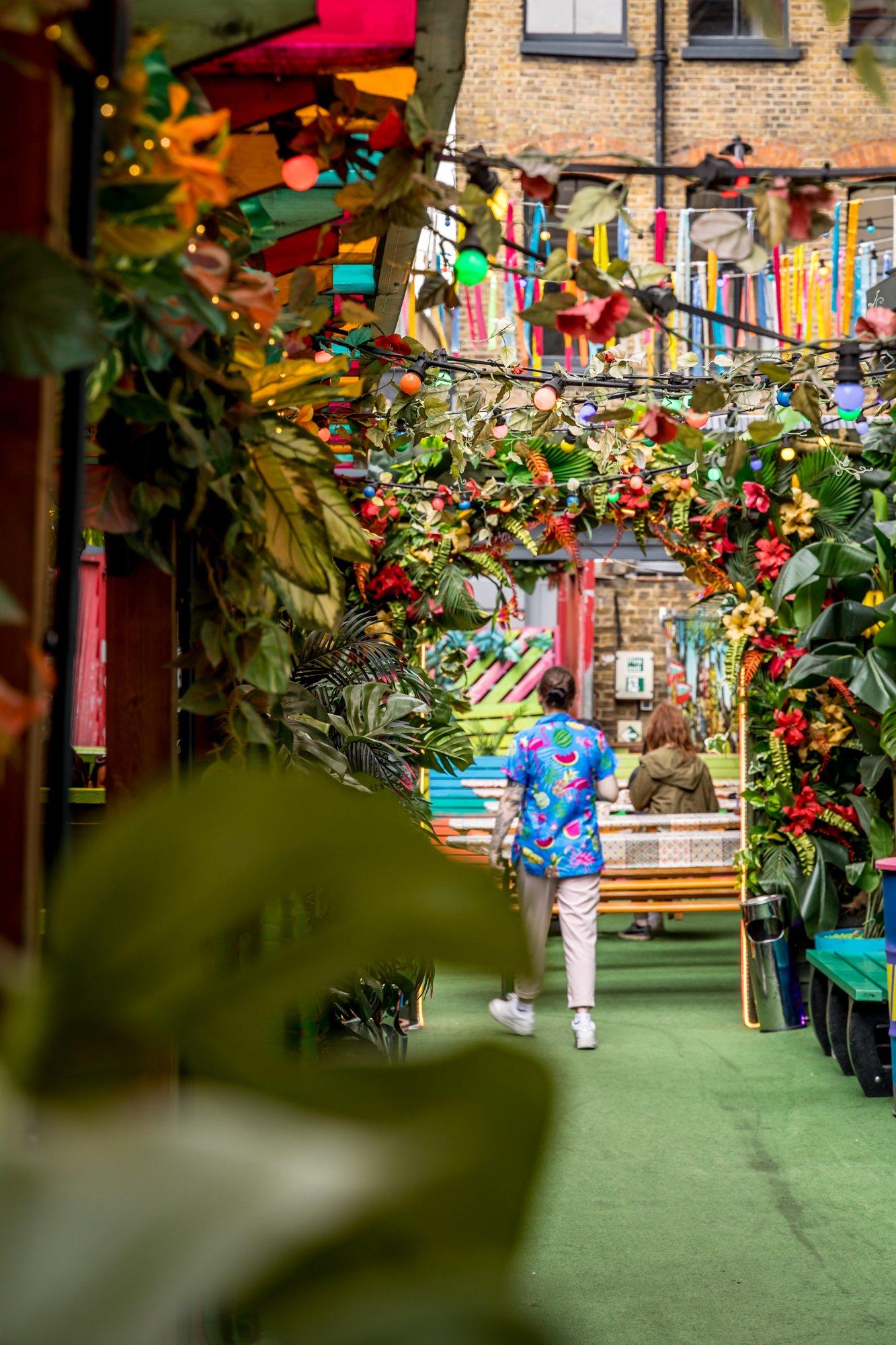 Person walking through a floral archway in Barrio, Shoreditch