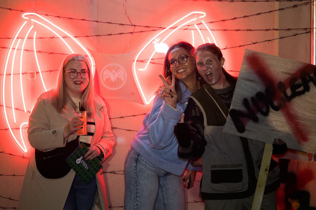 Three women standing in front of a neon wings sign smiling