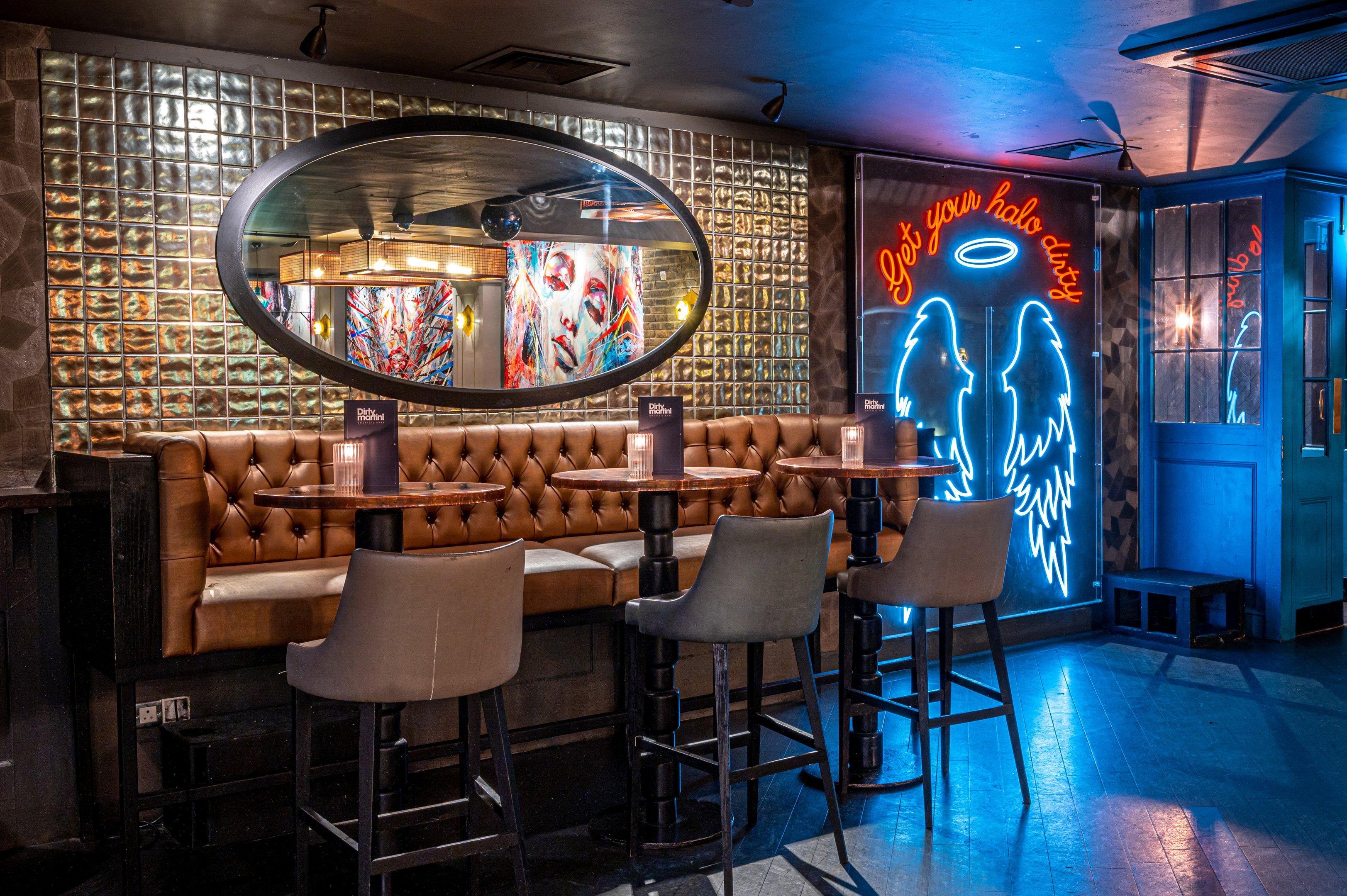 Interior shot of Dirty Martini Bishopsgate showing high seated tables and a neon sign