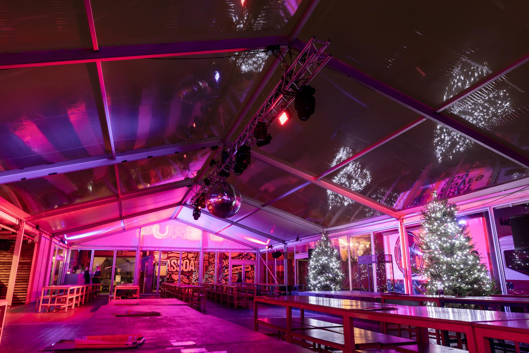 A heated marquee with bench seating and lit up Christmas trees