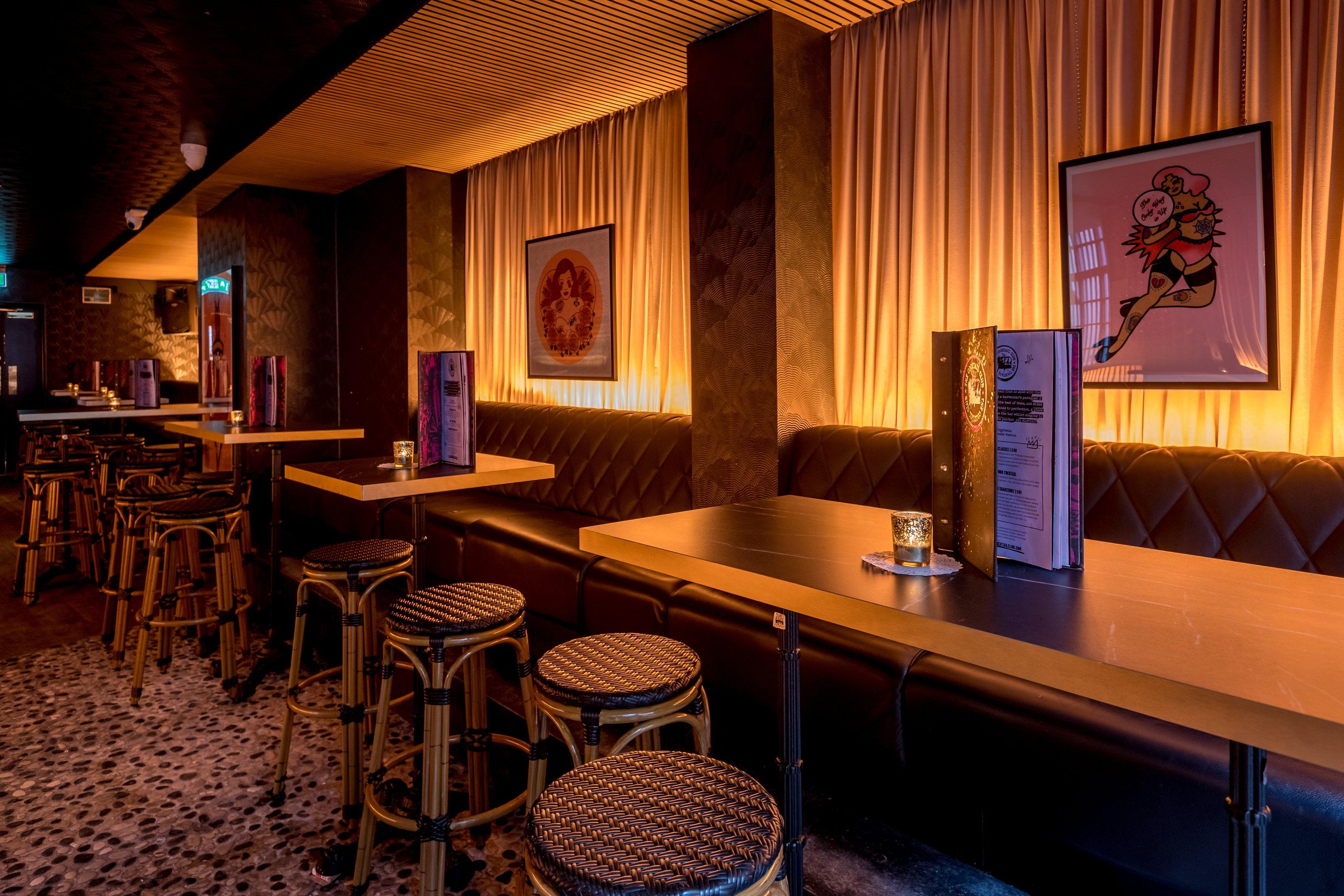 A bar area with black leather seats, draped curtains and mood lighting