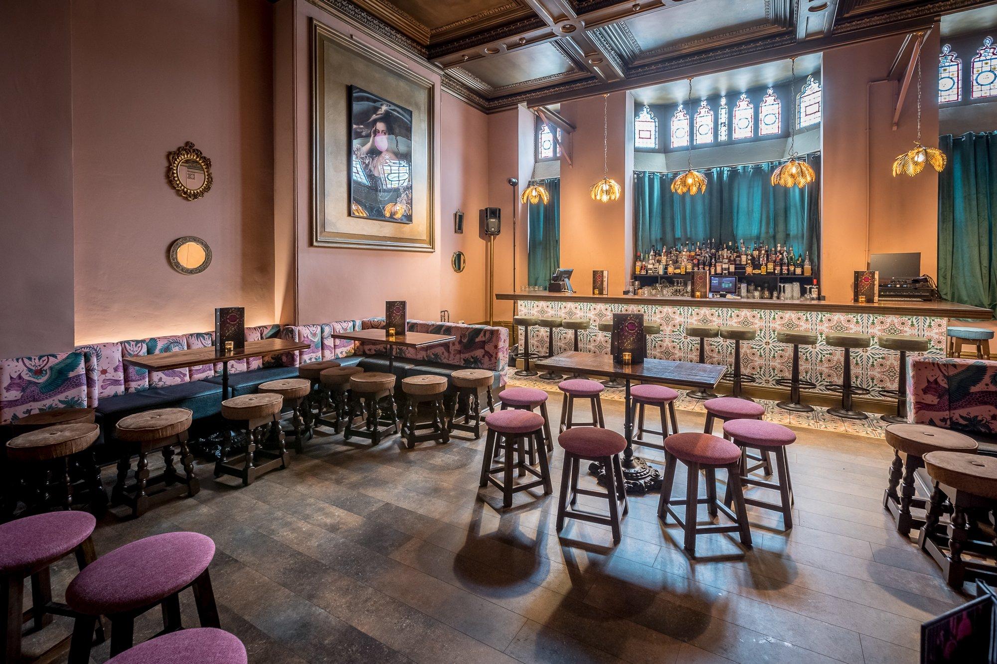 An opulent bar area with pink blush walls and velvet stool seats