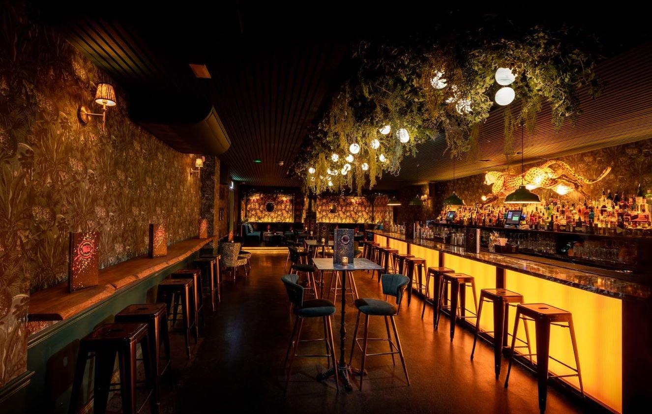 A long bar area with a garden trellis ceiling and bold floral wallpaper