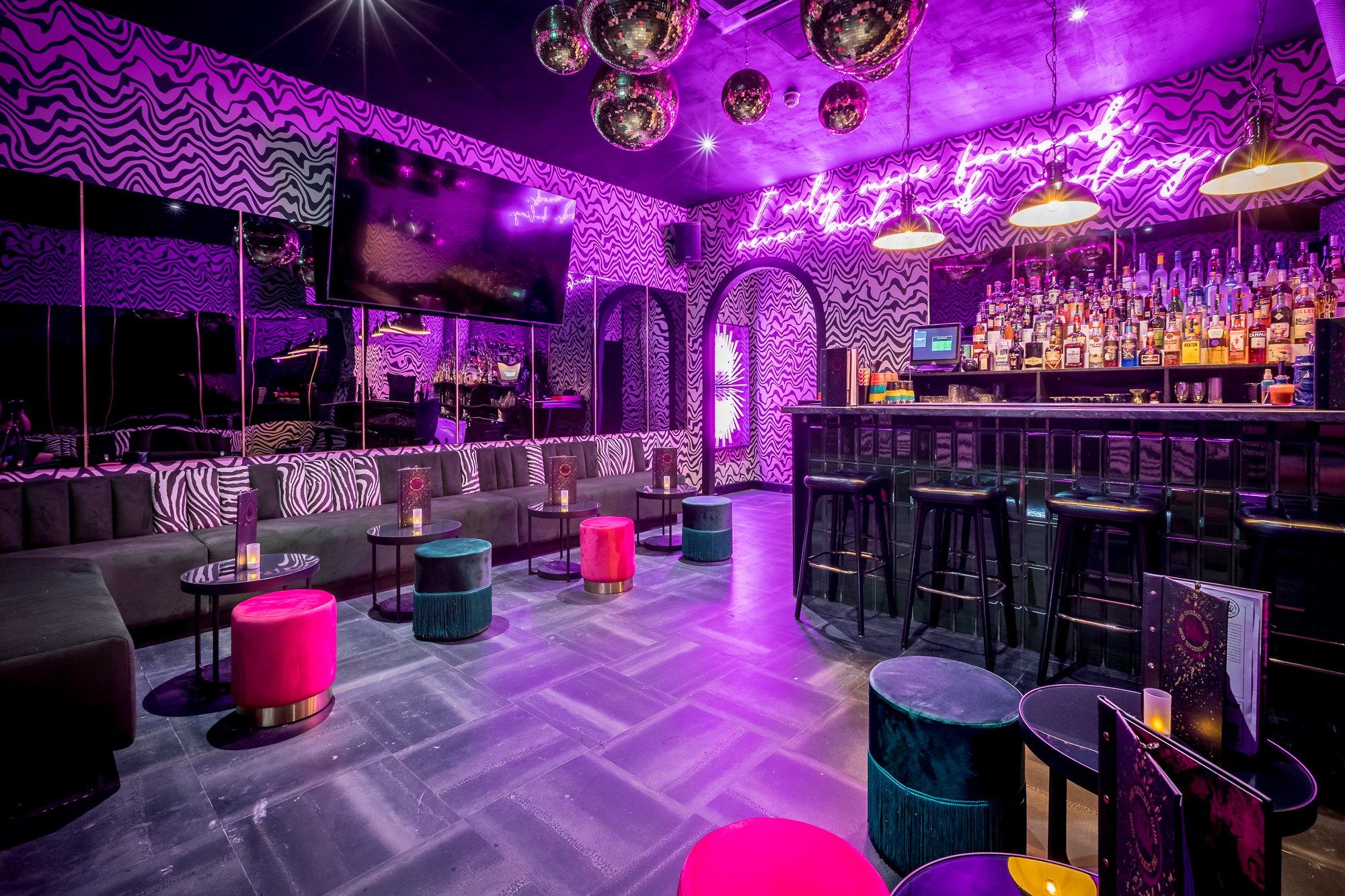 A neon lit private room with bold wallpaper and a karaoke screen