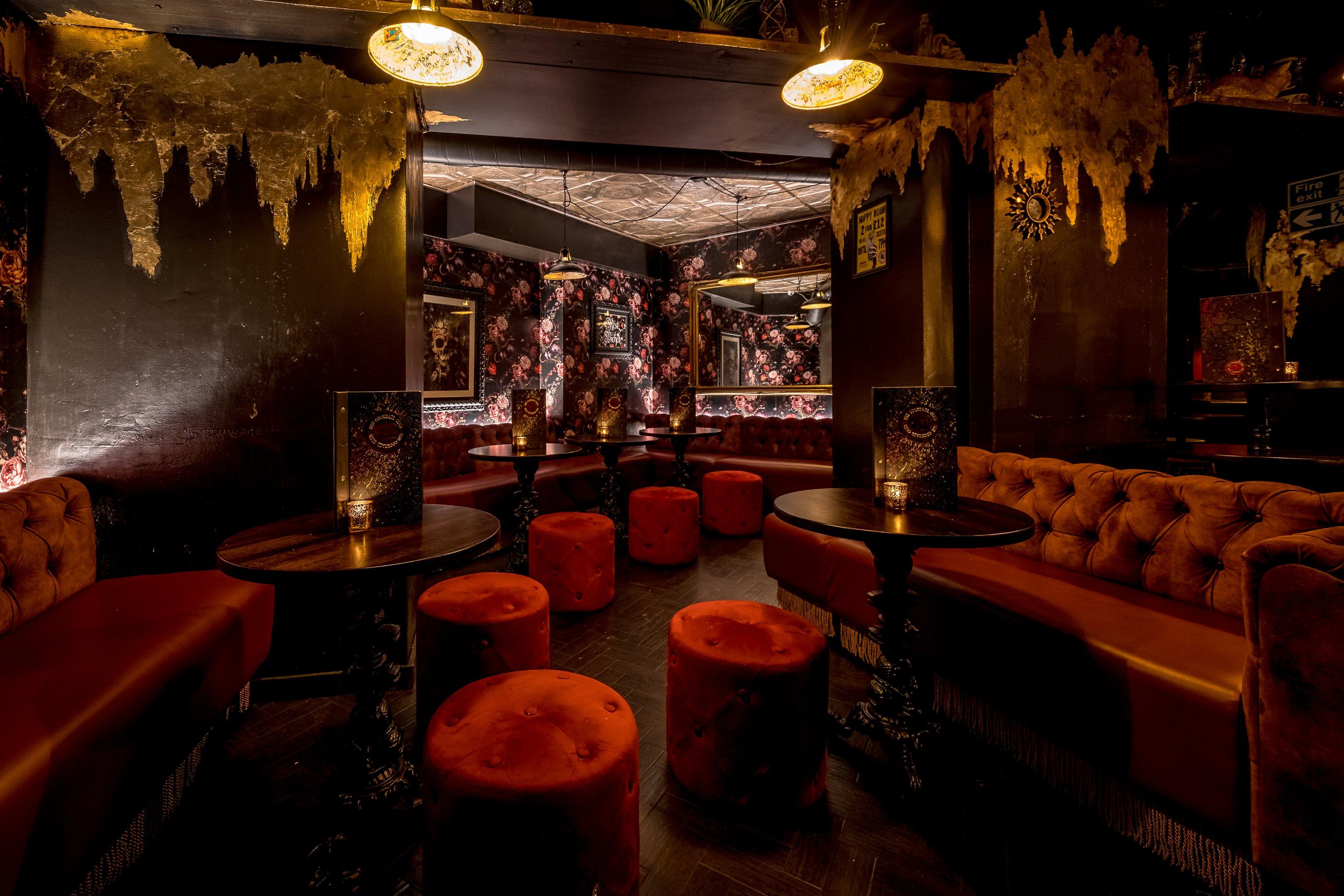 Velvet booth and stool seating area in a dimly lit bar with bold wallpapers