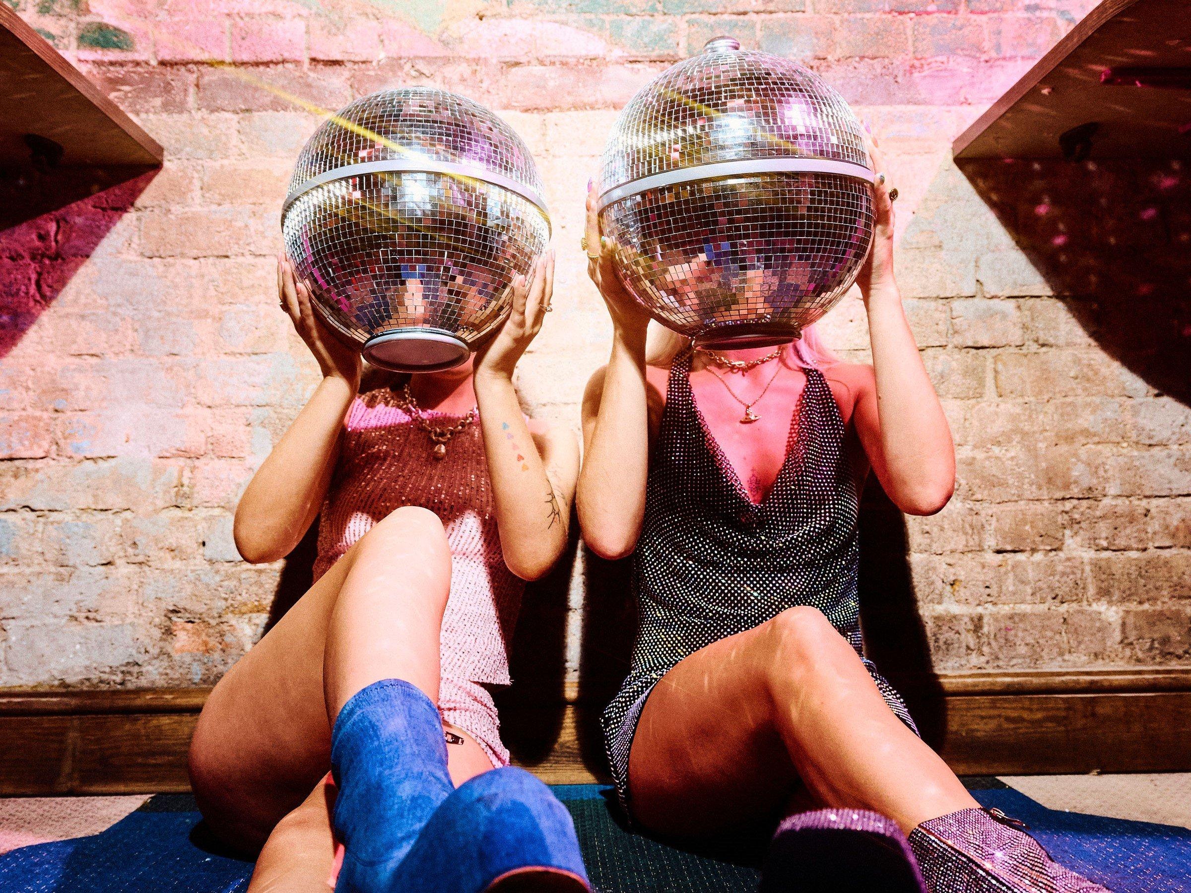 Two women sat on the ground posing and holding Disco Ball Sharers