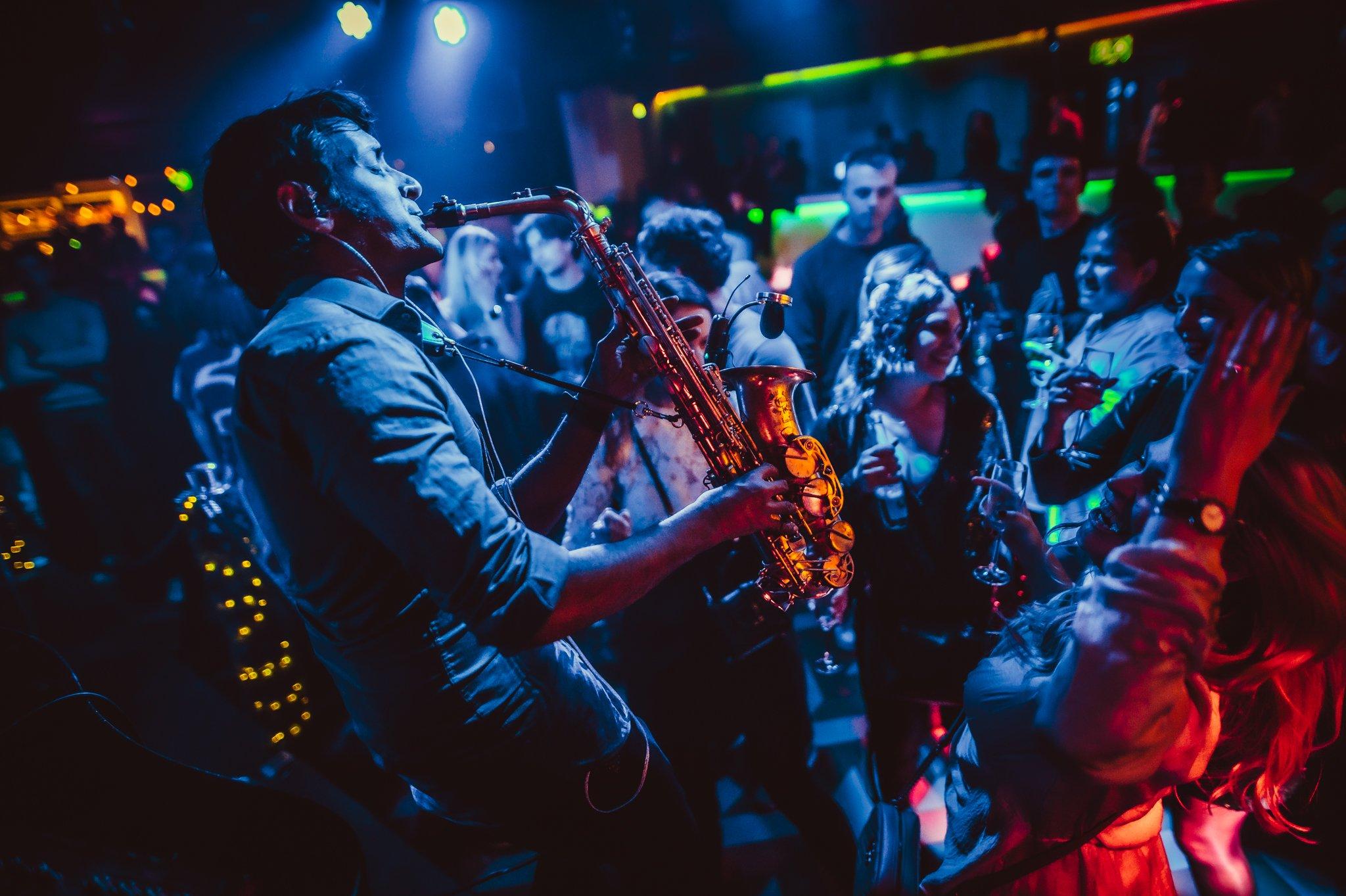 Musician performing live with a Saxophone to a crowd of guests in Piano Works