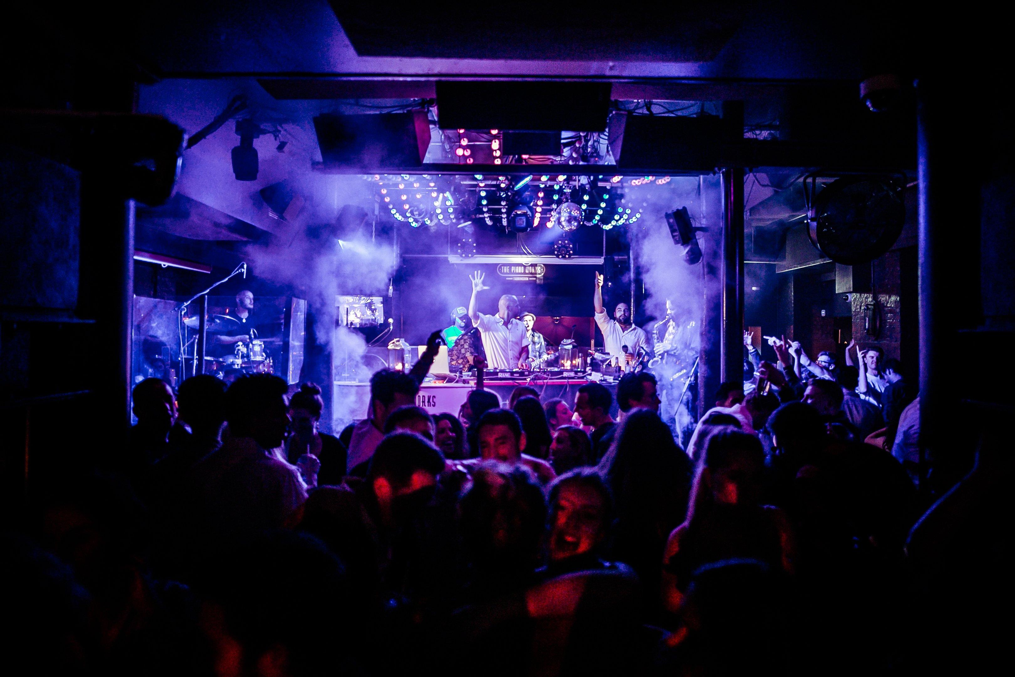 A stage with a live DJ and customers dancing in The Piano Works