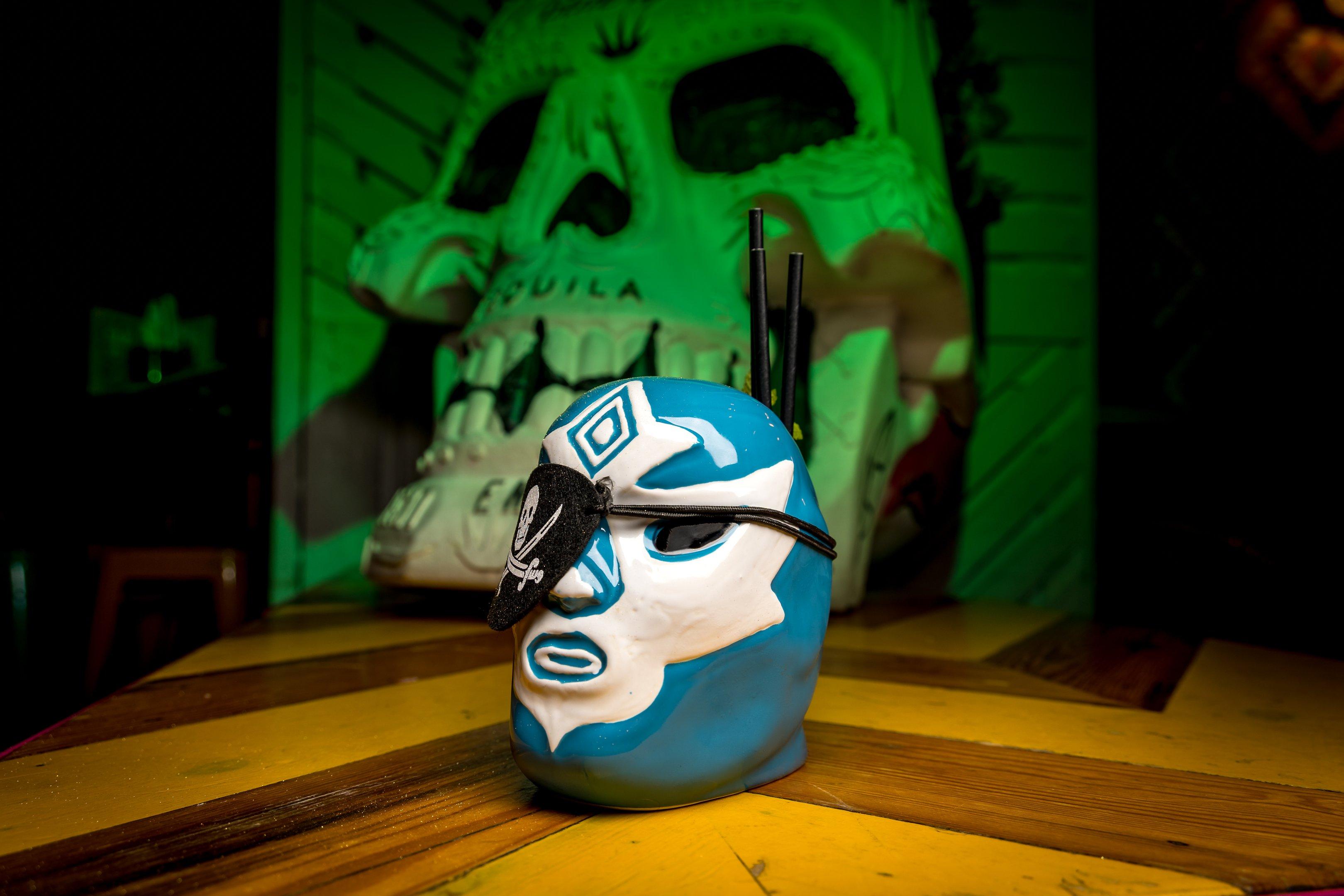 A cocktail in a ceramic mask glass with a pirates eye patch as a garnish