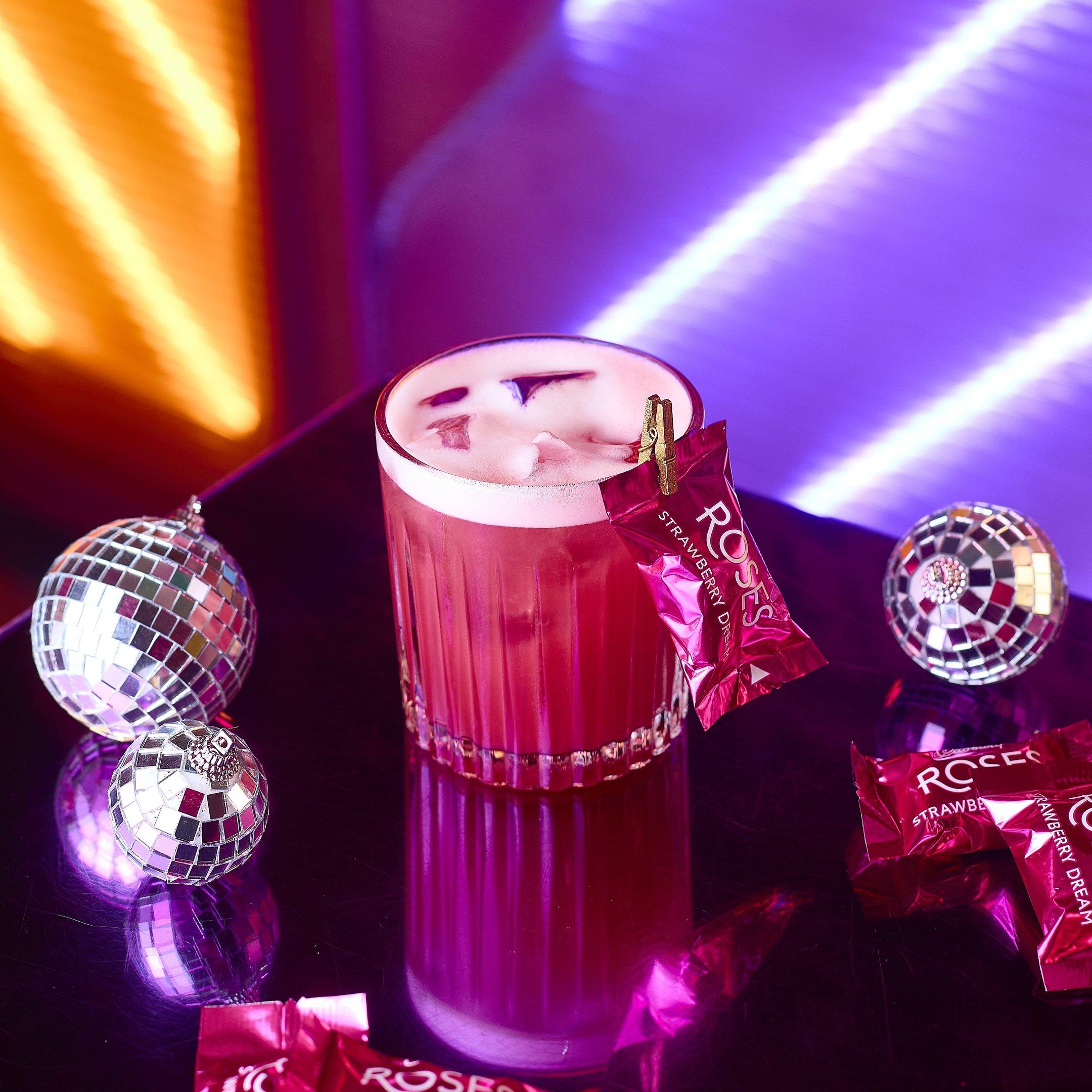 Image of a pink festive cocktail with a Roses chocolate garnish