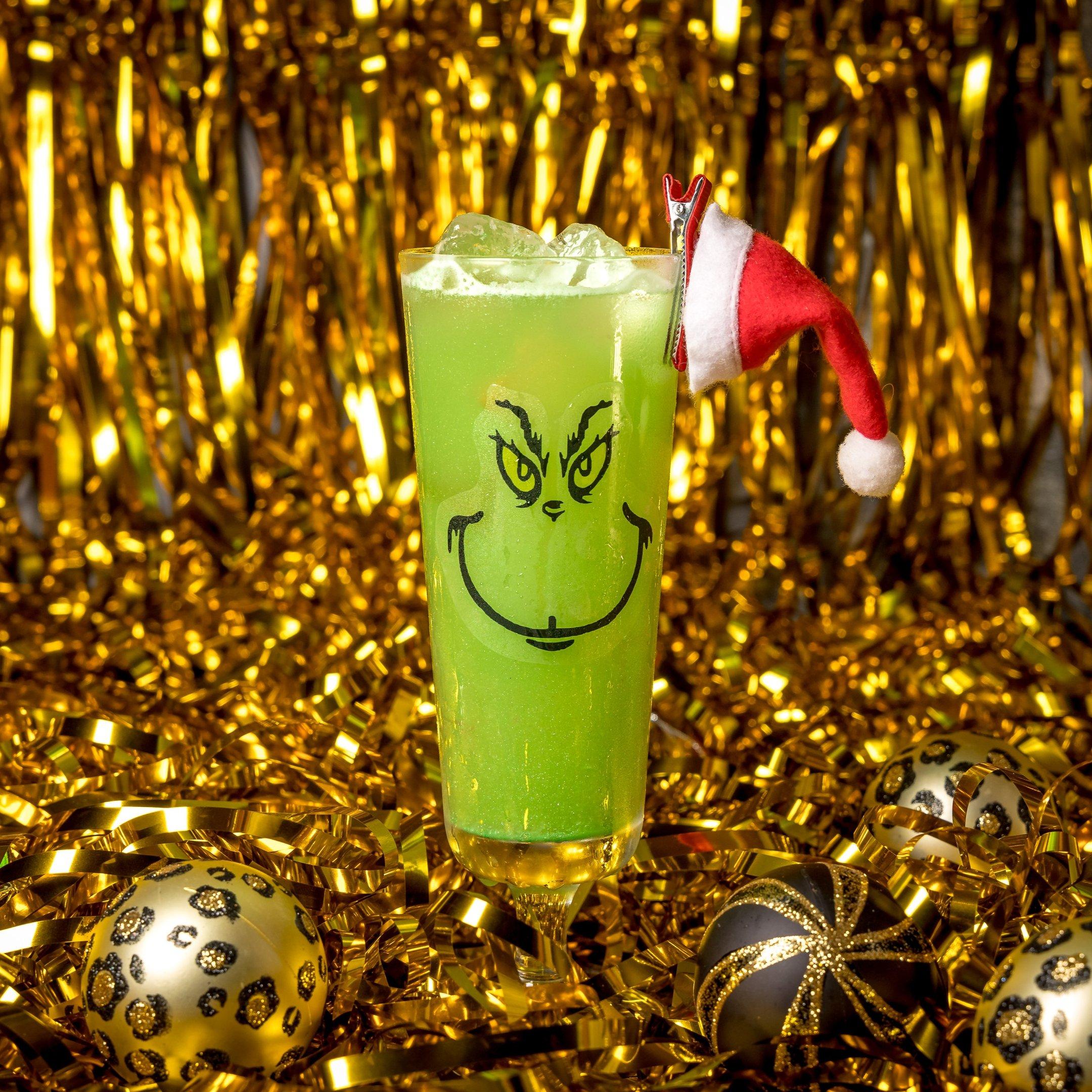 A green cocktail with a Grinch face decoration on the glass