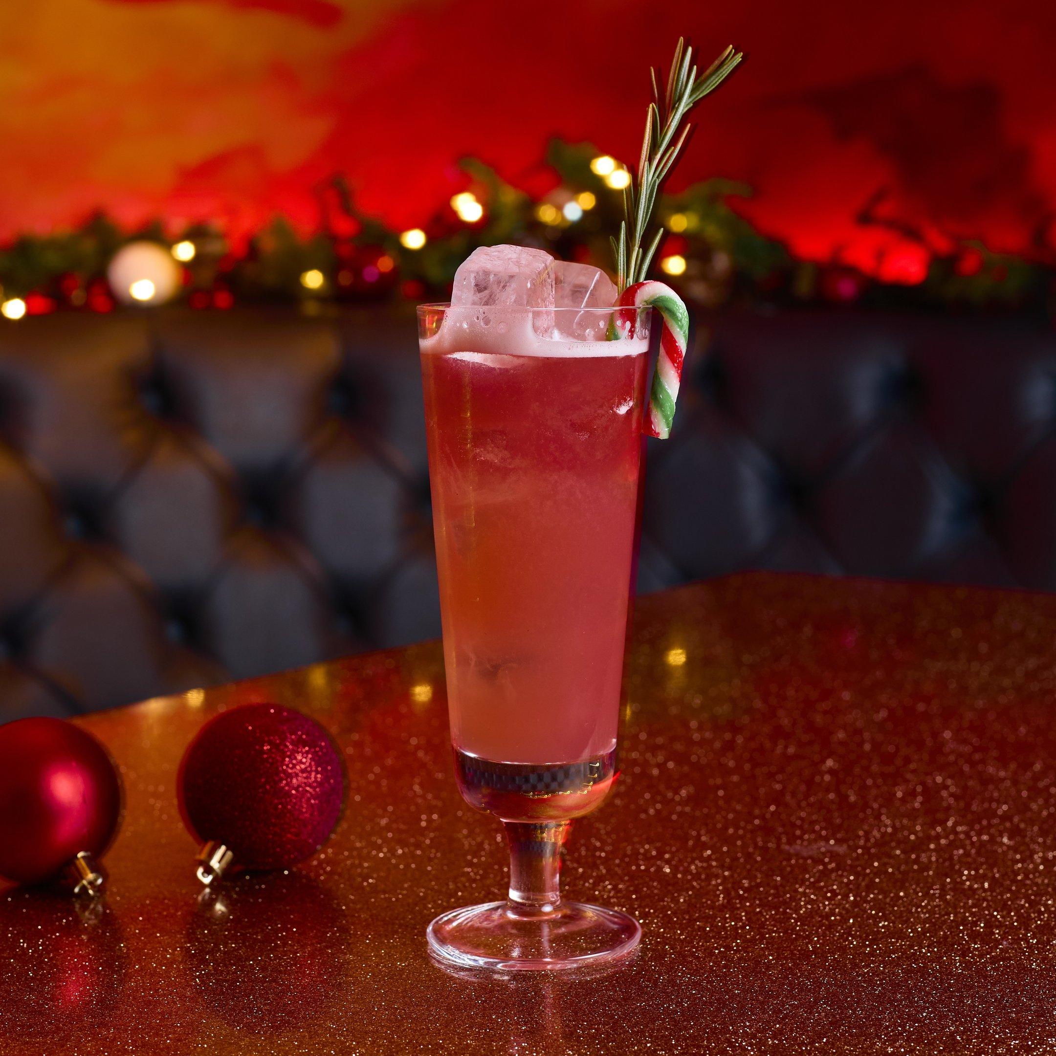 A red cocktail in a tall glass with a mini candy cane garnish