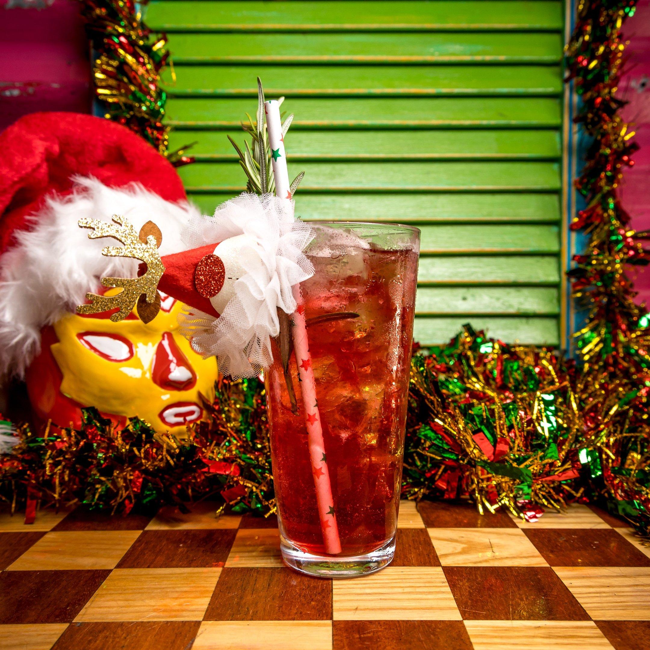 A red cocktail in a tall glass with a mini Christmas hat garnish