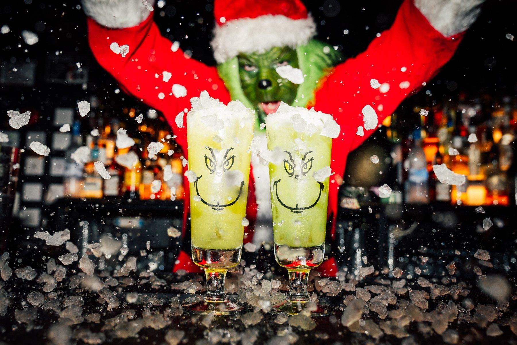 A Grinch pouring ice over 2 Grinch cocktails at The Cocktail Club