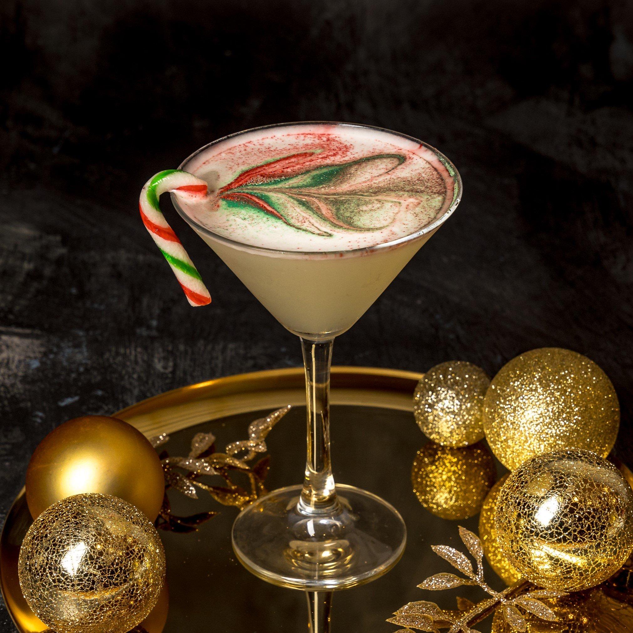 A Christmas cocktail with a candy cane garnish and topped with edible glitter