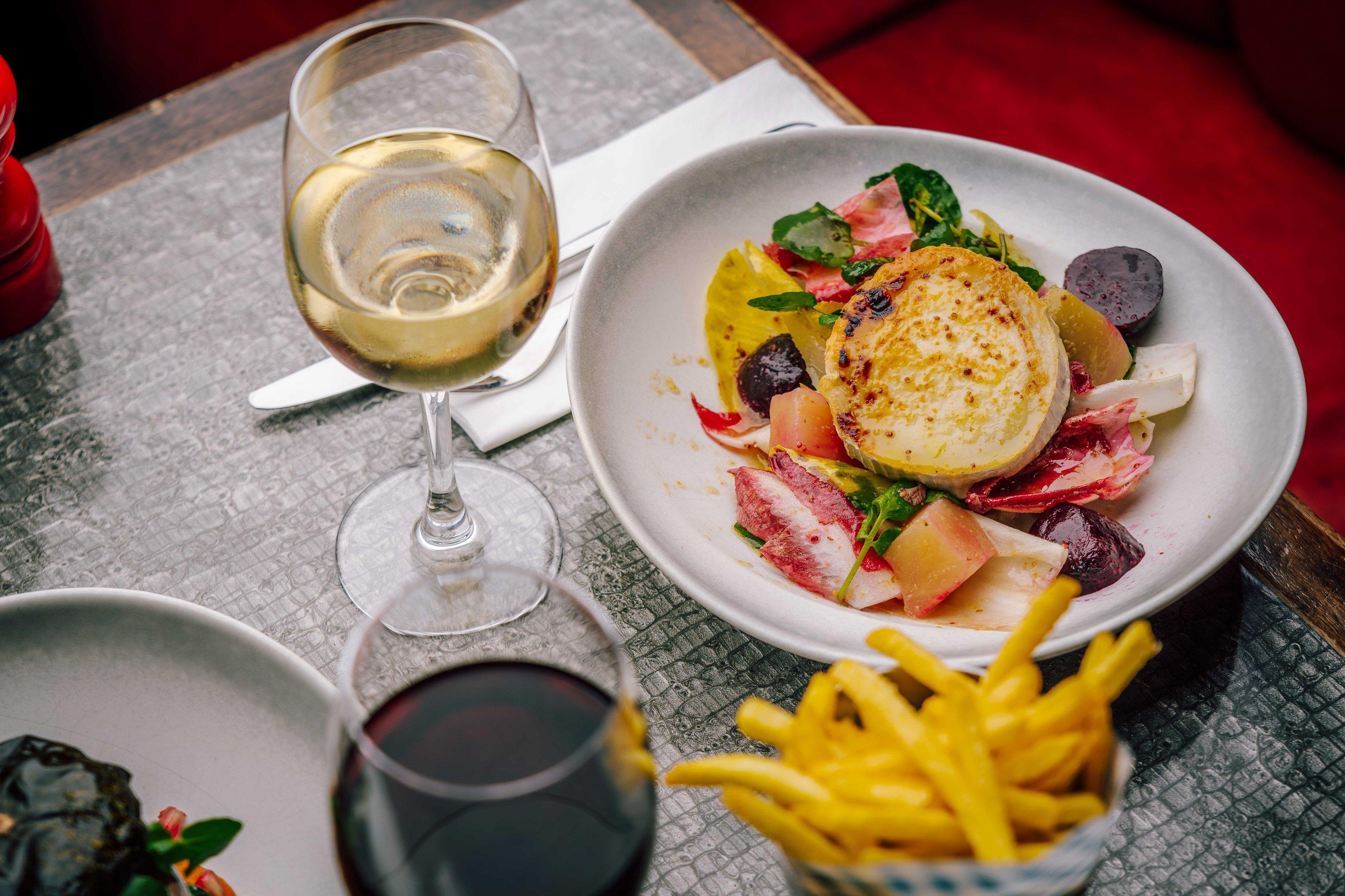 A dining table with a main meal and glasses of wine at Tuttons