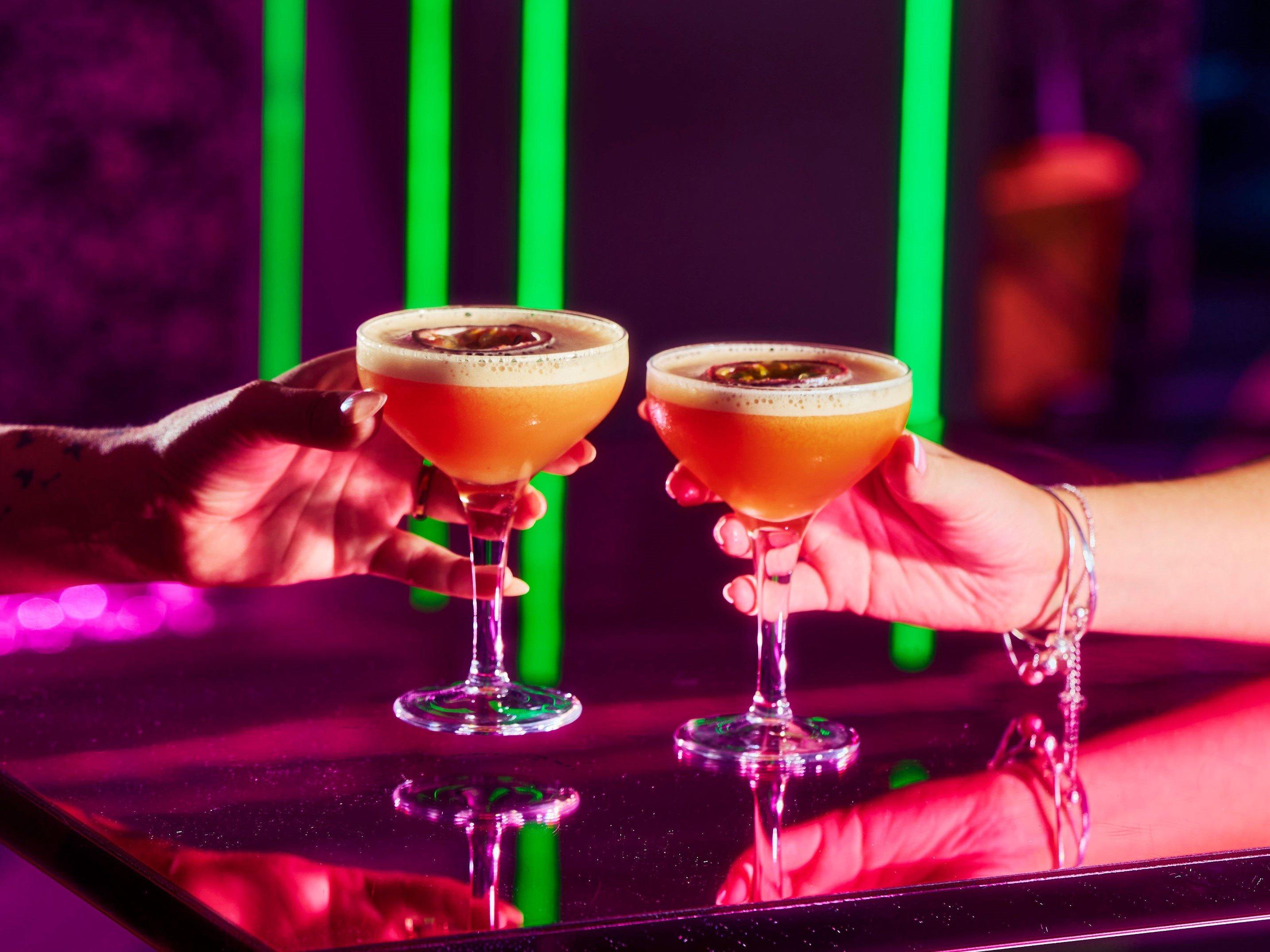 Guests holding pornstar martini cocktails over a table