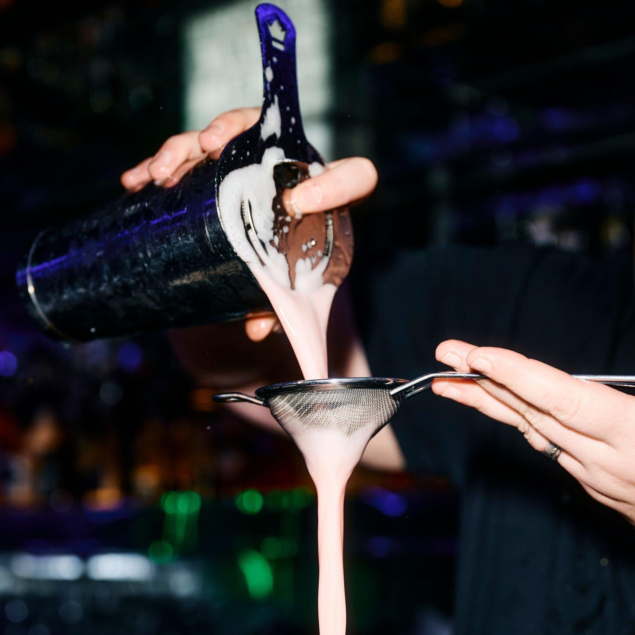 A bartender pouring a cocktail through a strain into a glass in Tonight Josephine