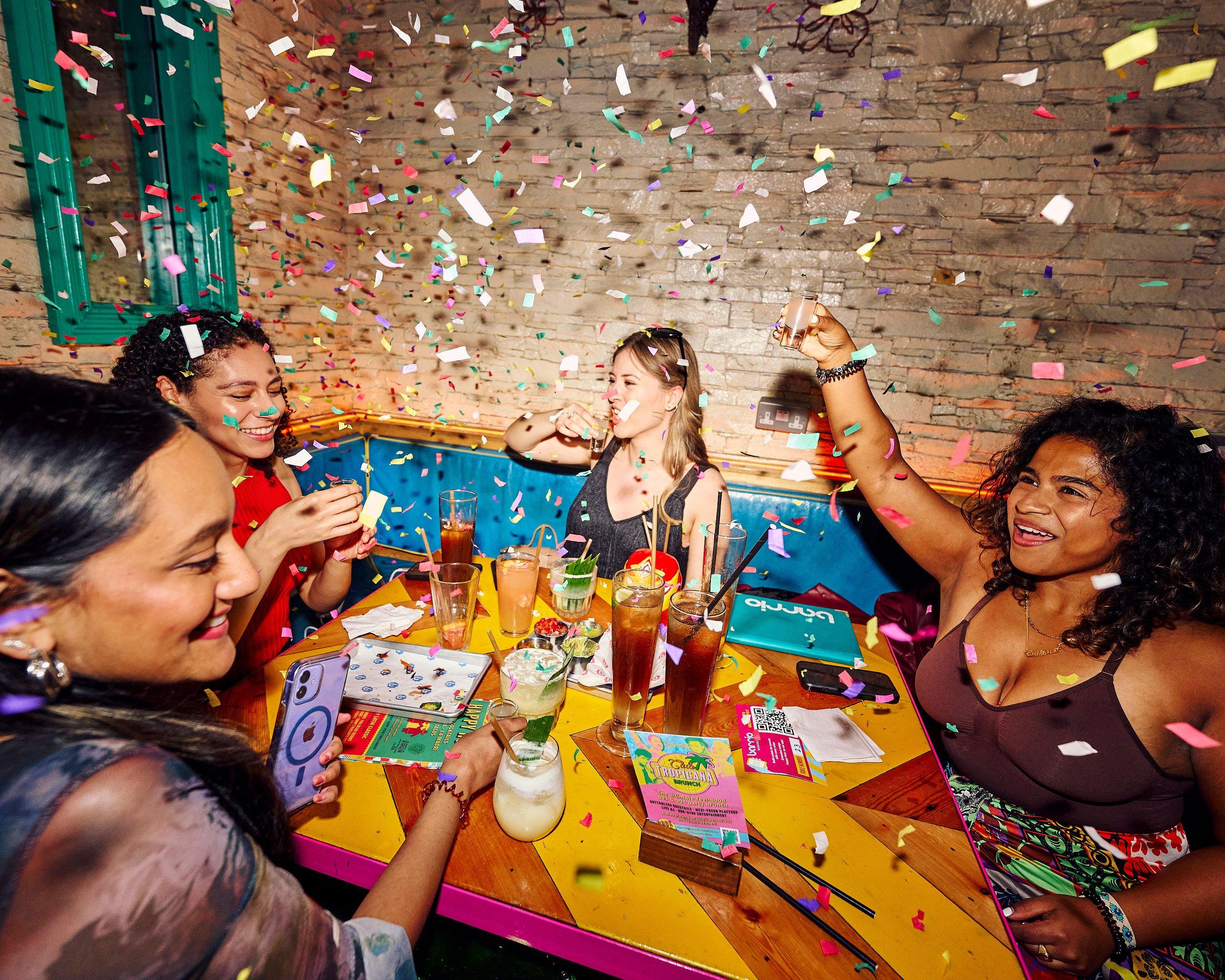 Women drinking and celebrating with confetti at a table in Barrio