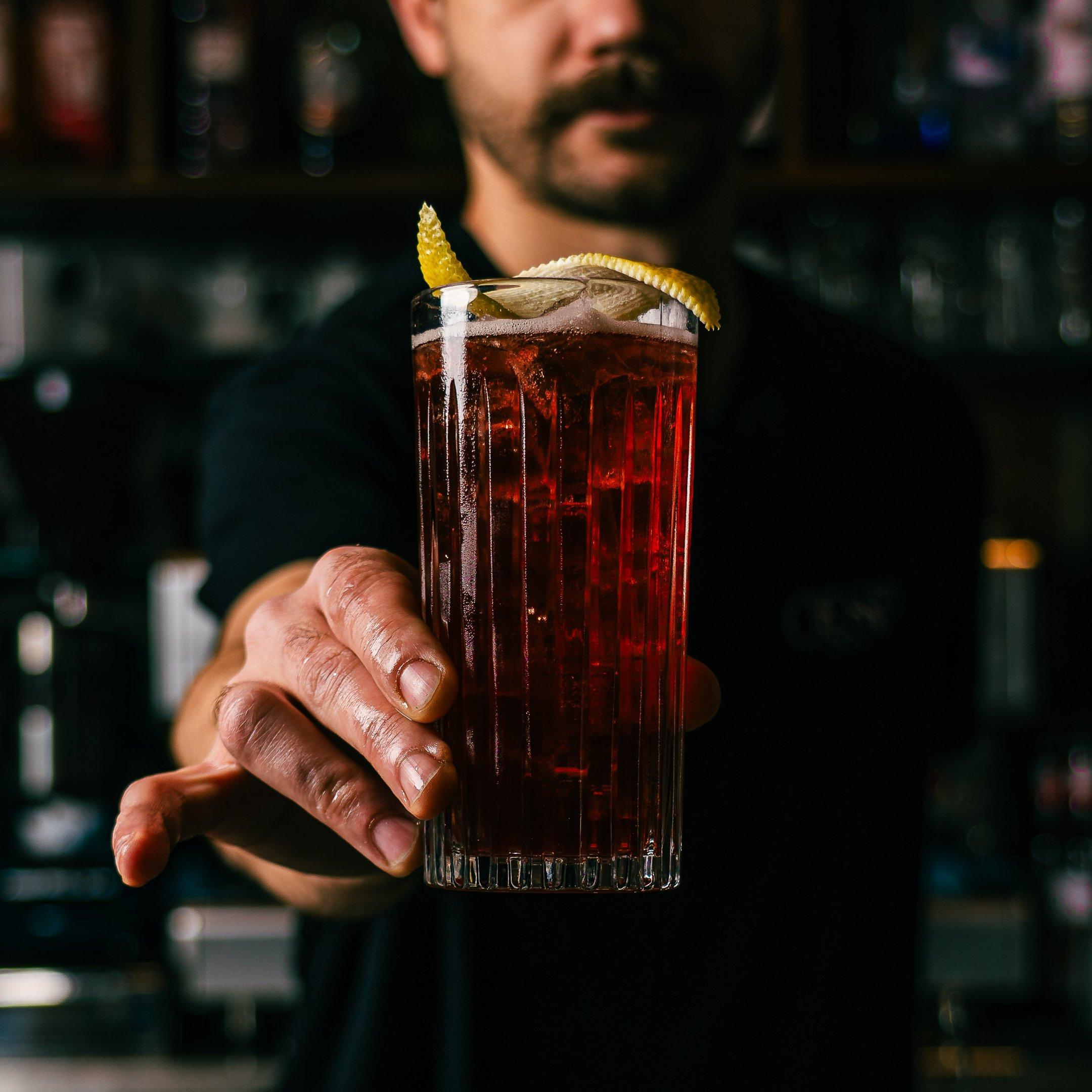 A bartender holding a Mountain Berry Hiball mocktail at Tuttons