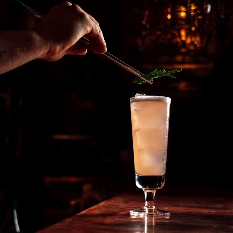 A bartender garnishing a mocktail in a tall glass