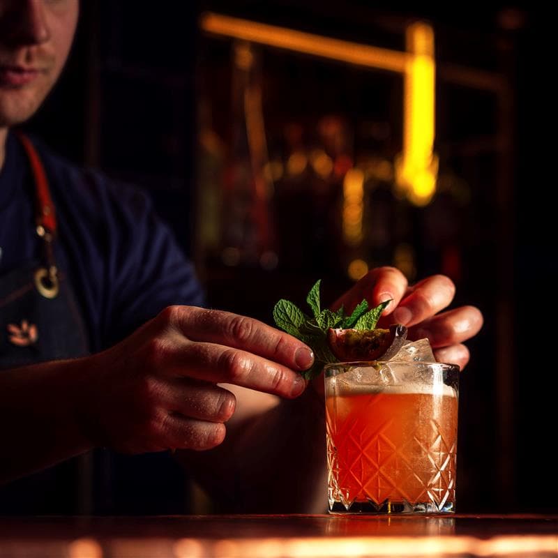 A bartender garnishing a mocktail in a short glass with passion fruit