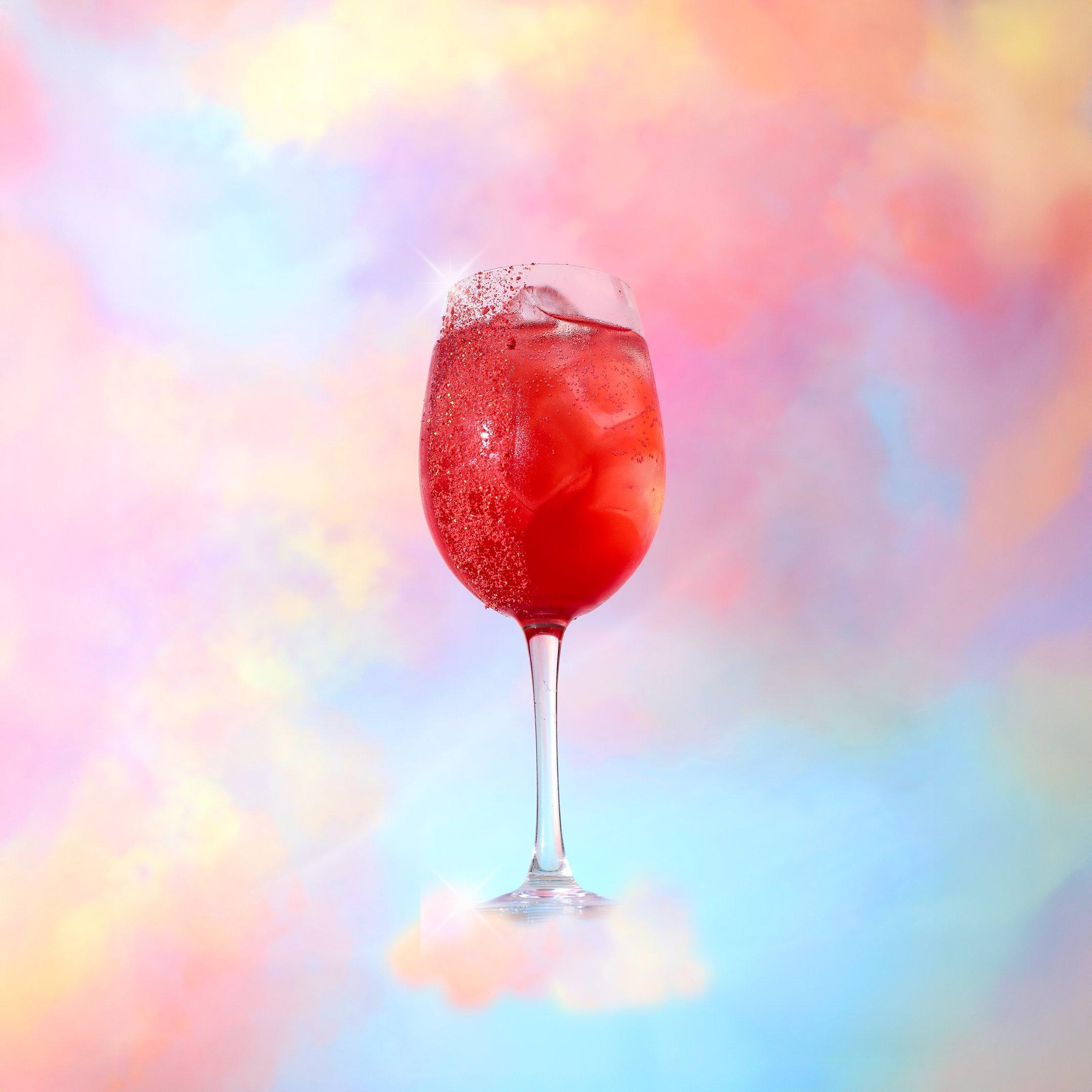 A Strawberry Light Spritz Tonight Josephine mocktail in front of a cloud background