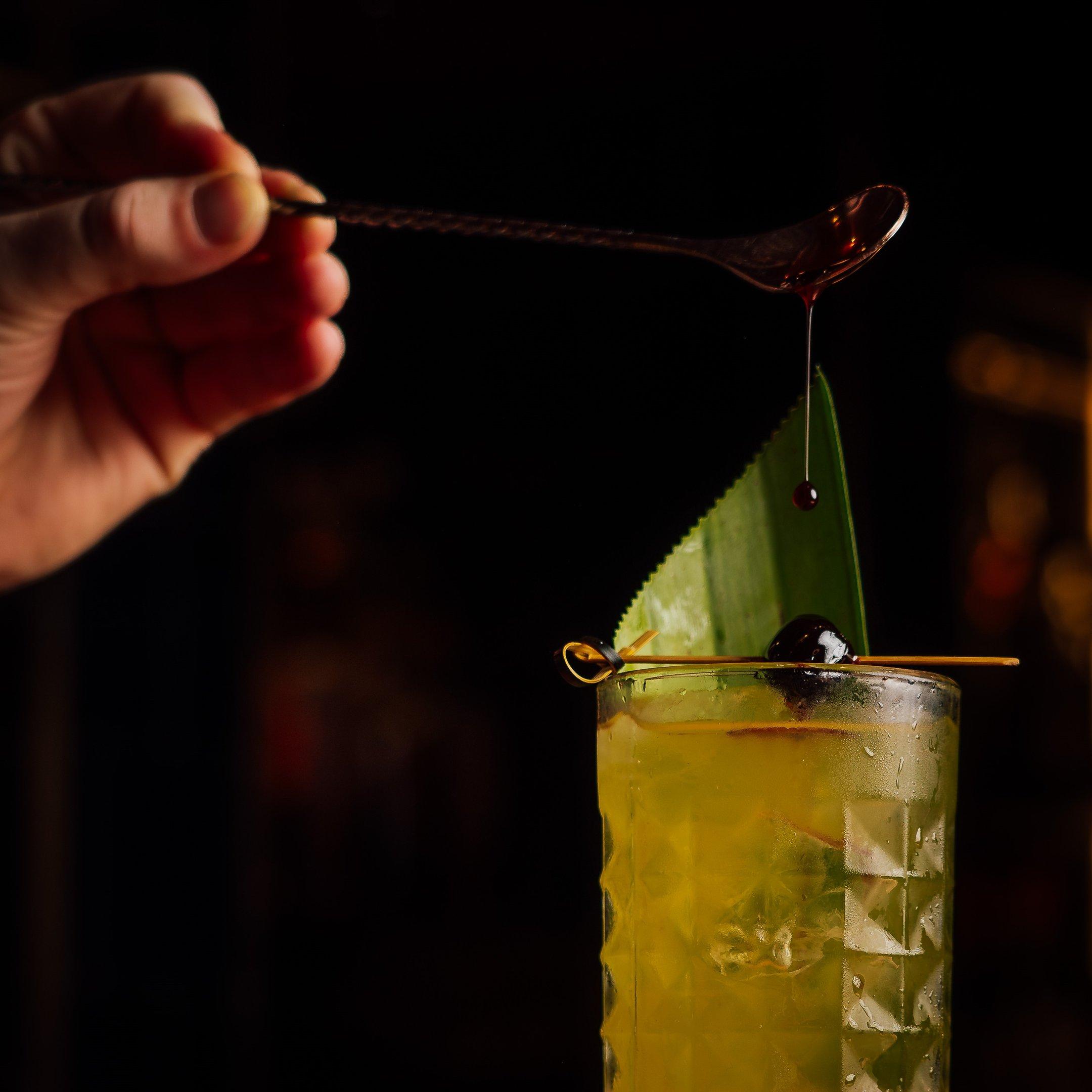 A hand pouring an ingredient into a Roasted Pineapple Colada cocktail at The Escapologist