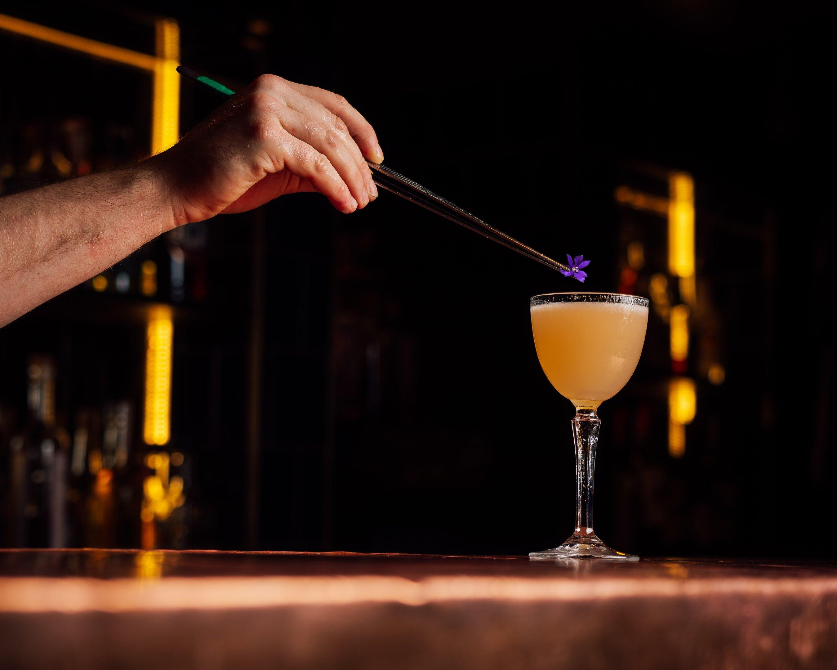 A bartender garnishing a Lychee & Lace cocktail with an edible flower at The Escapologist