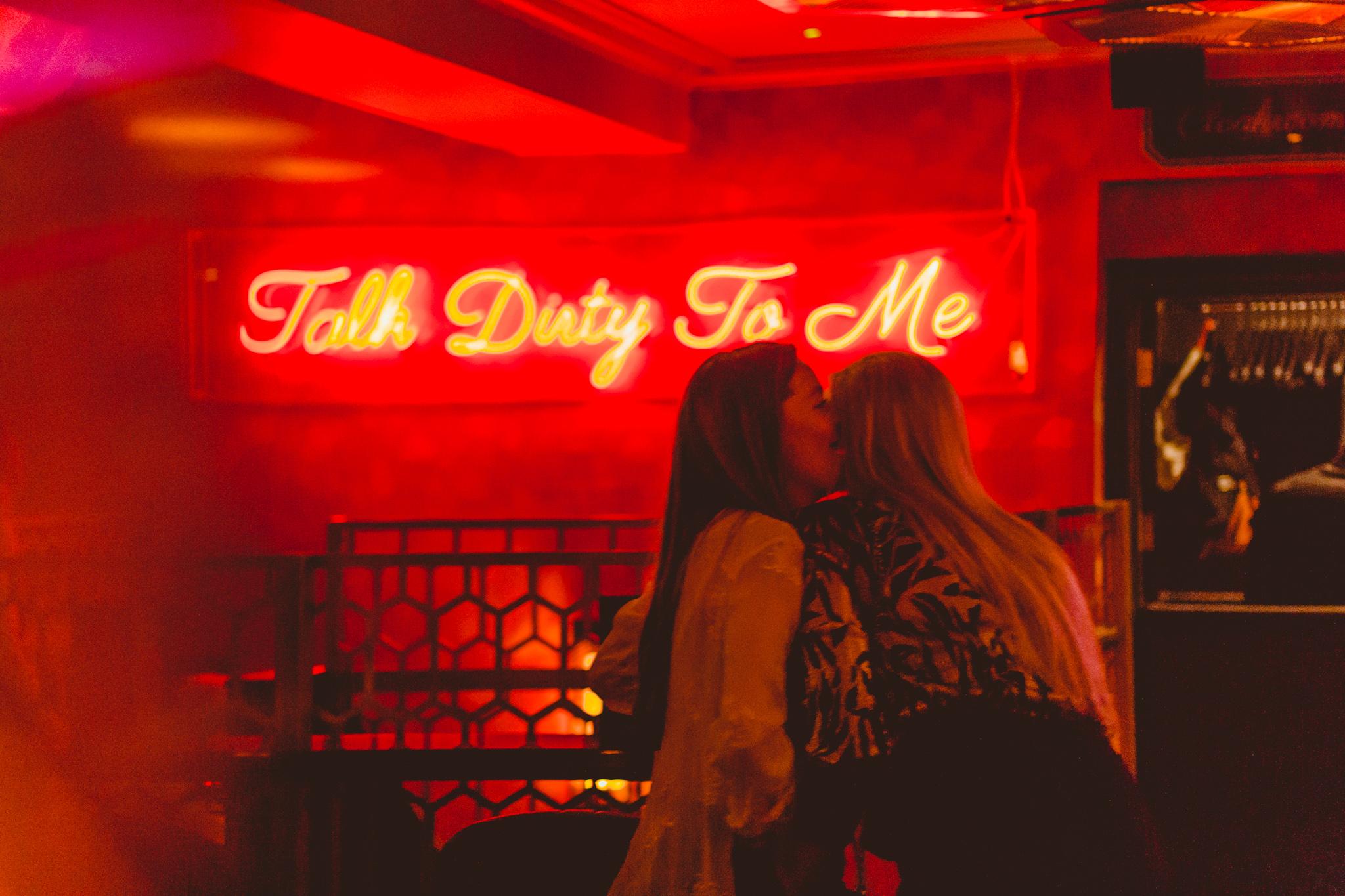 Guests whispering in front of a neon sign in Dirty Martini