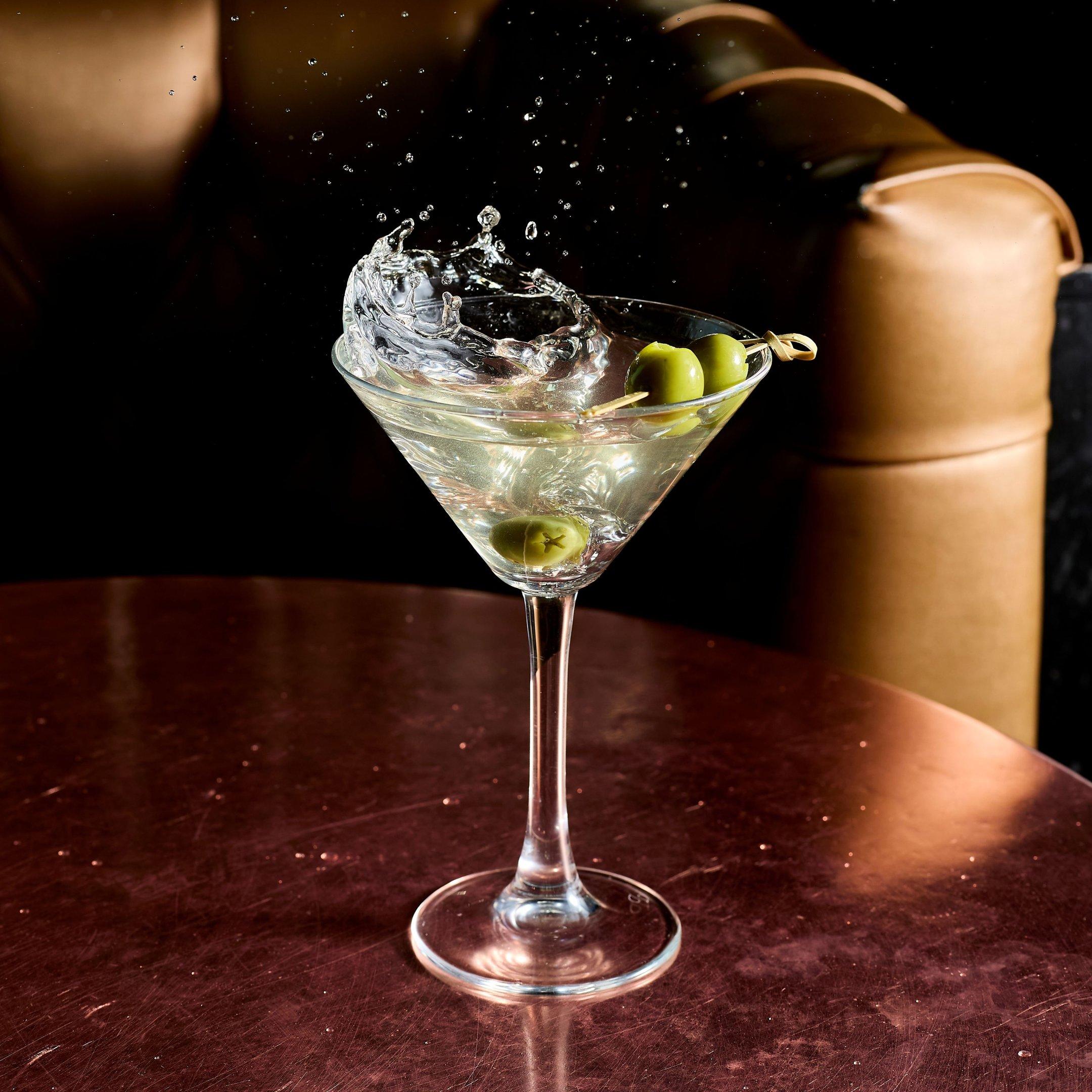 A Dirty Martini cocktail with an olive garnish splashing into the glass