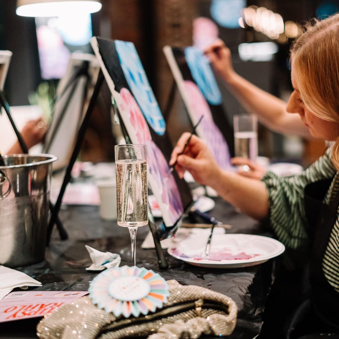 A women painting on a canvas whilst enjoying a glass of prosecco