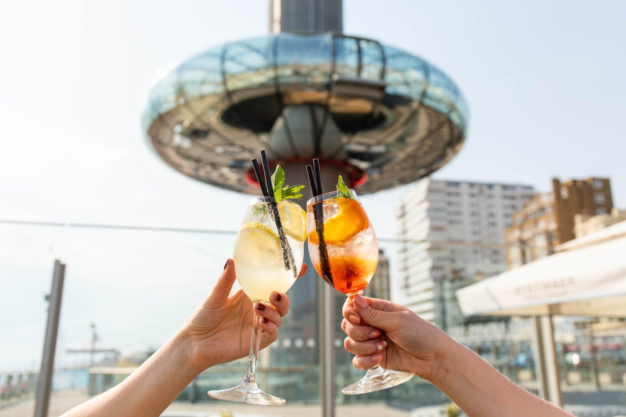 Two cocktails being held in front of the Brighton i360 Pod