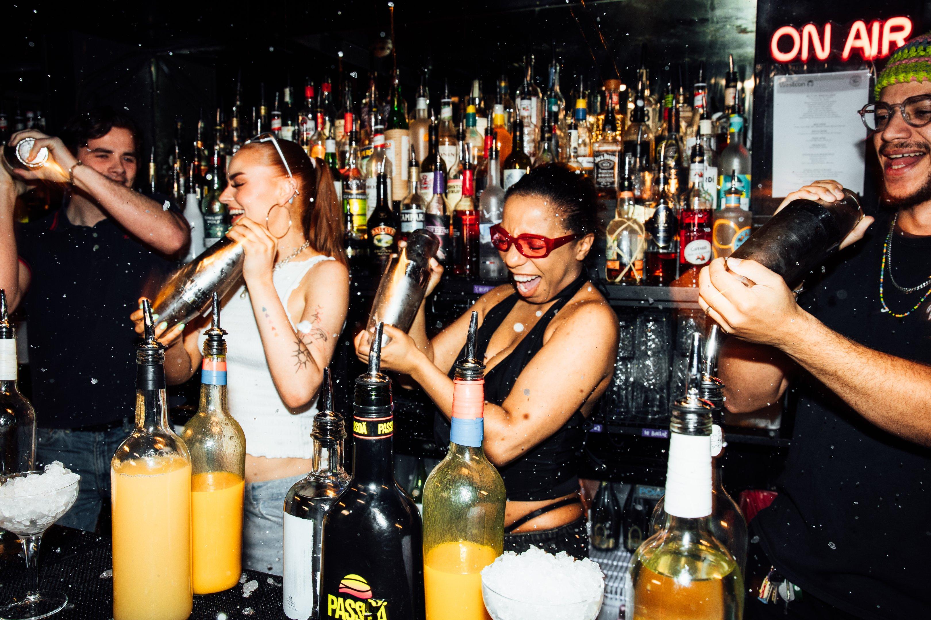 Guests behind the bar shaking cocktail shakers as they participate in a cocktail masterclass session at The Cocktail Club