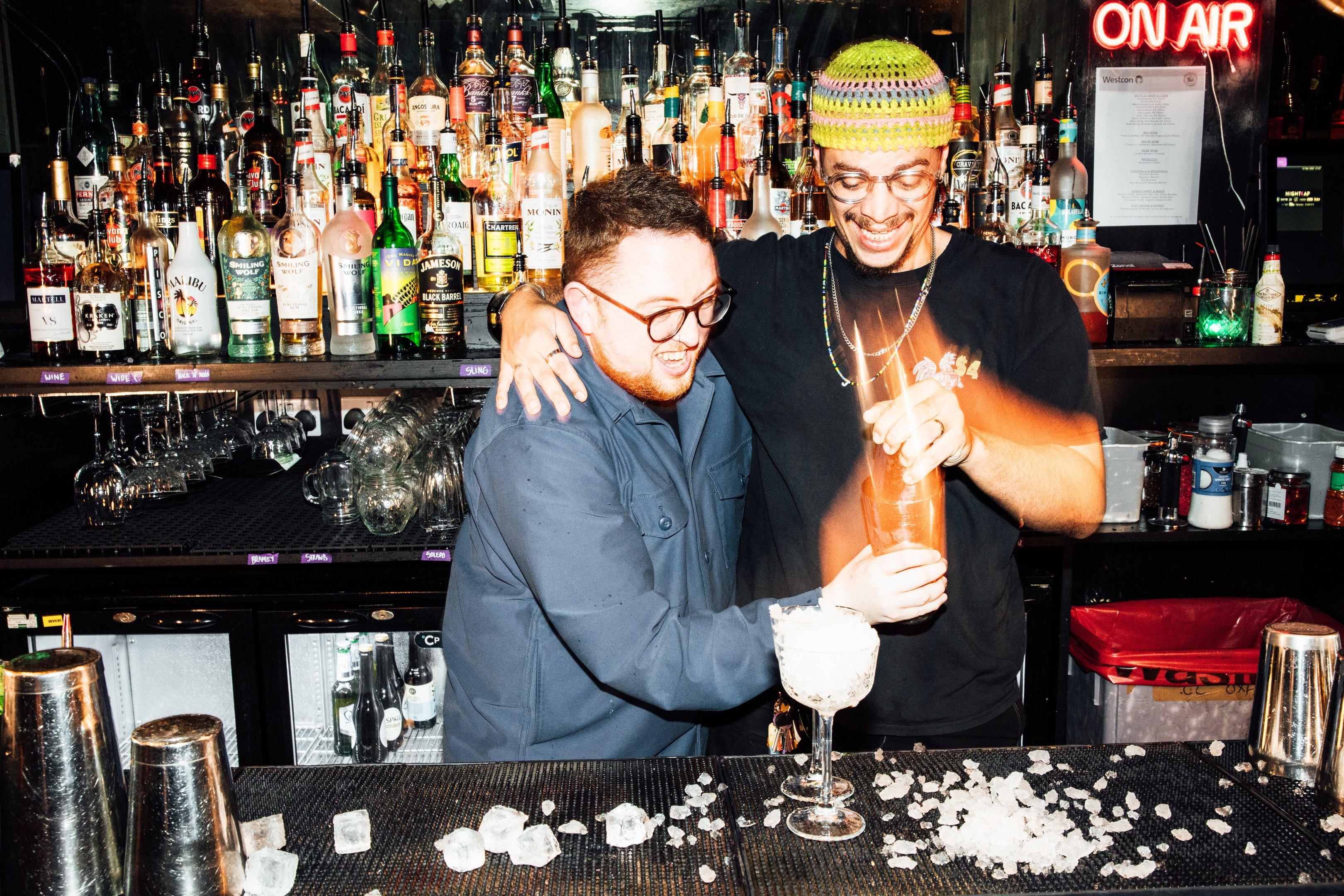 Two guests behind the bar in The Cocktail Club trying to make a cocktail with one arm around each other as part of the Daiquiri Challenge