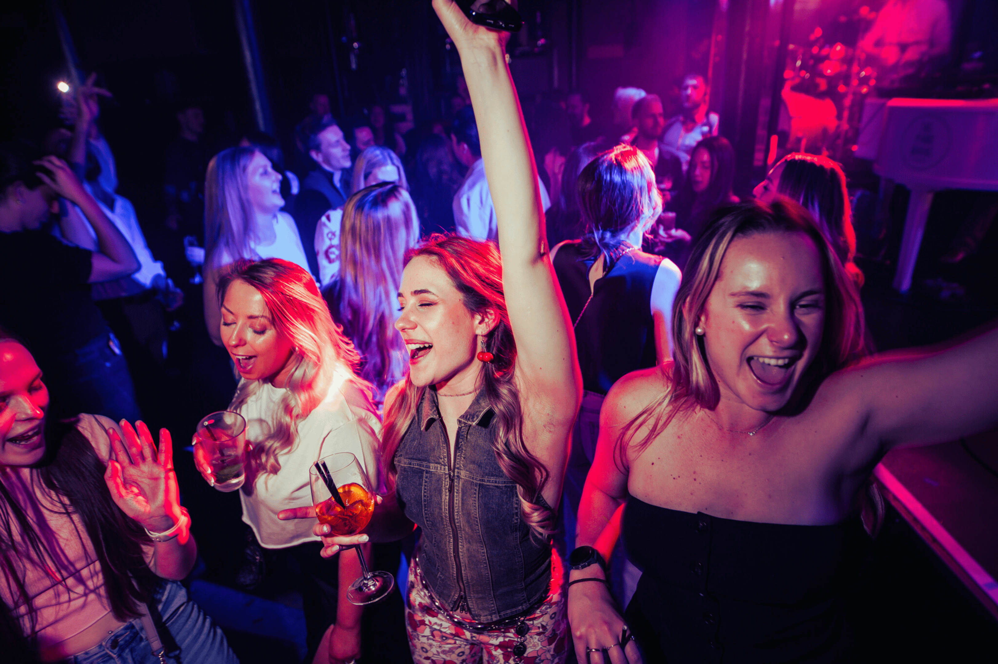An image focusing on three women dancing in a crowd with drinks in their hands at The Piano Works