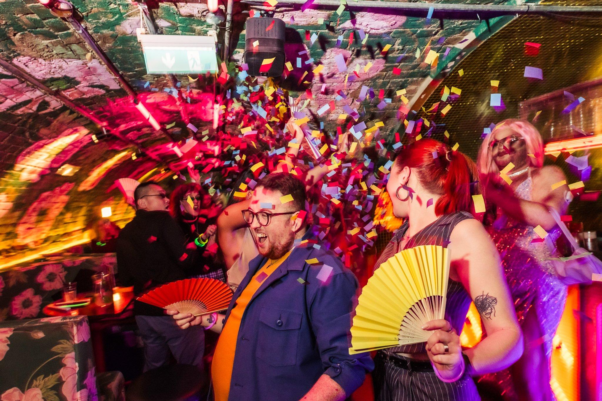 Guests dancing with multicoloured confetti falling around them in Blame Gloria