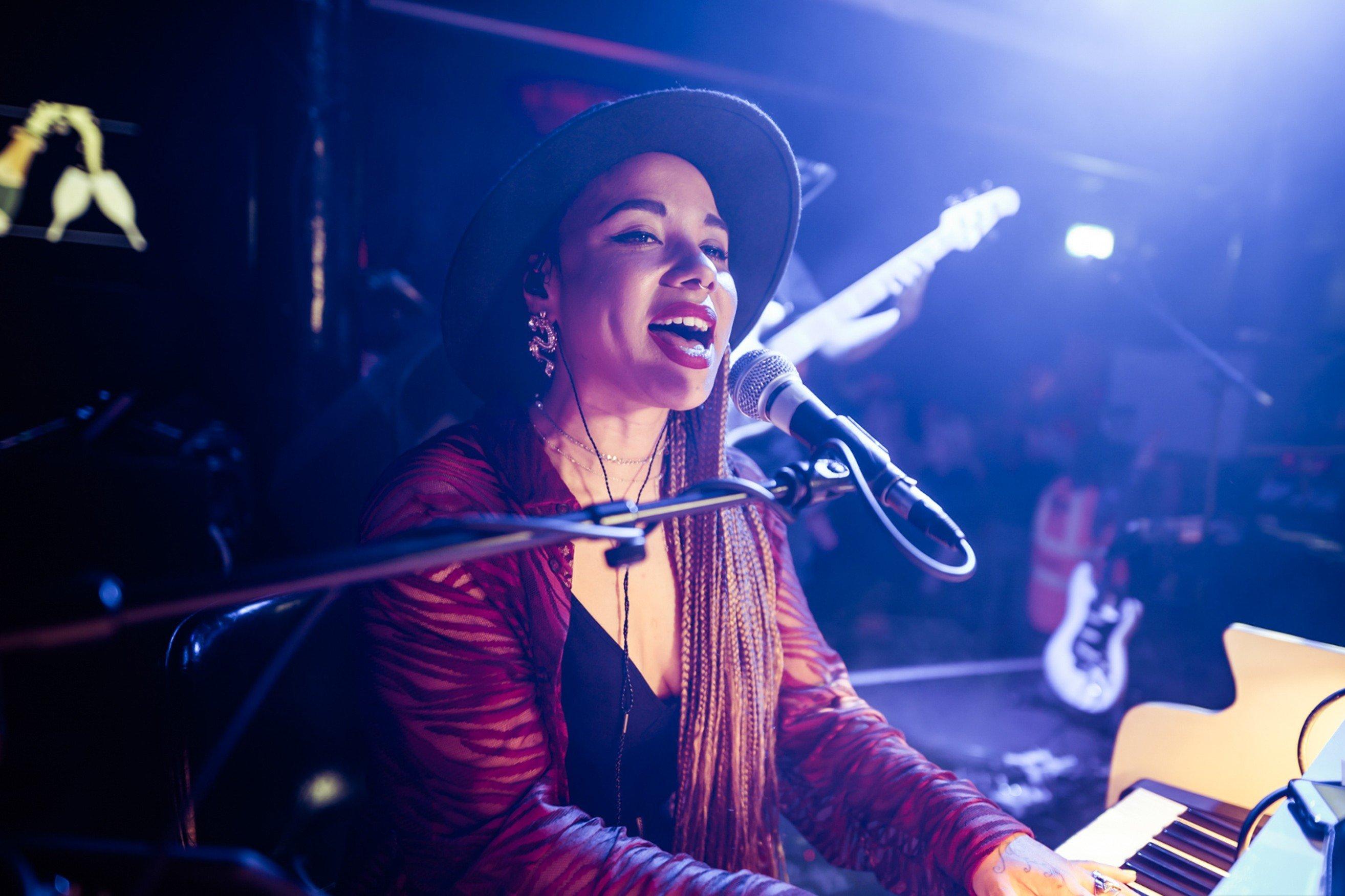 A woman playing the piano and singing on a stage in The Piano Works