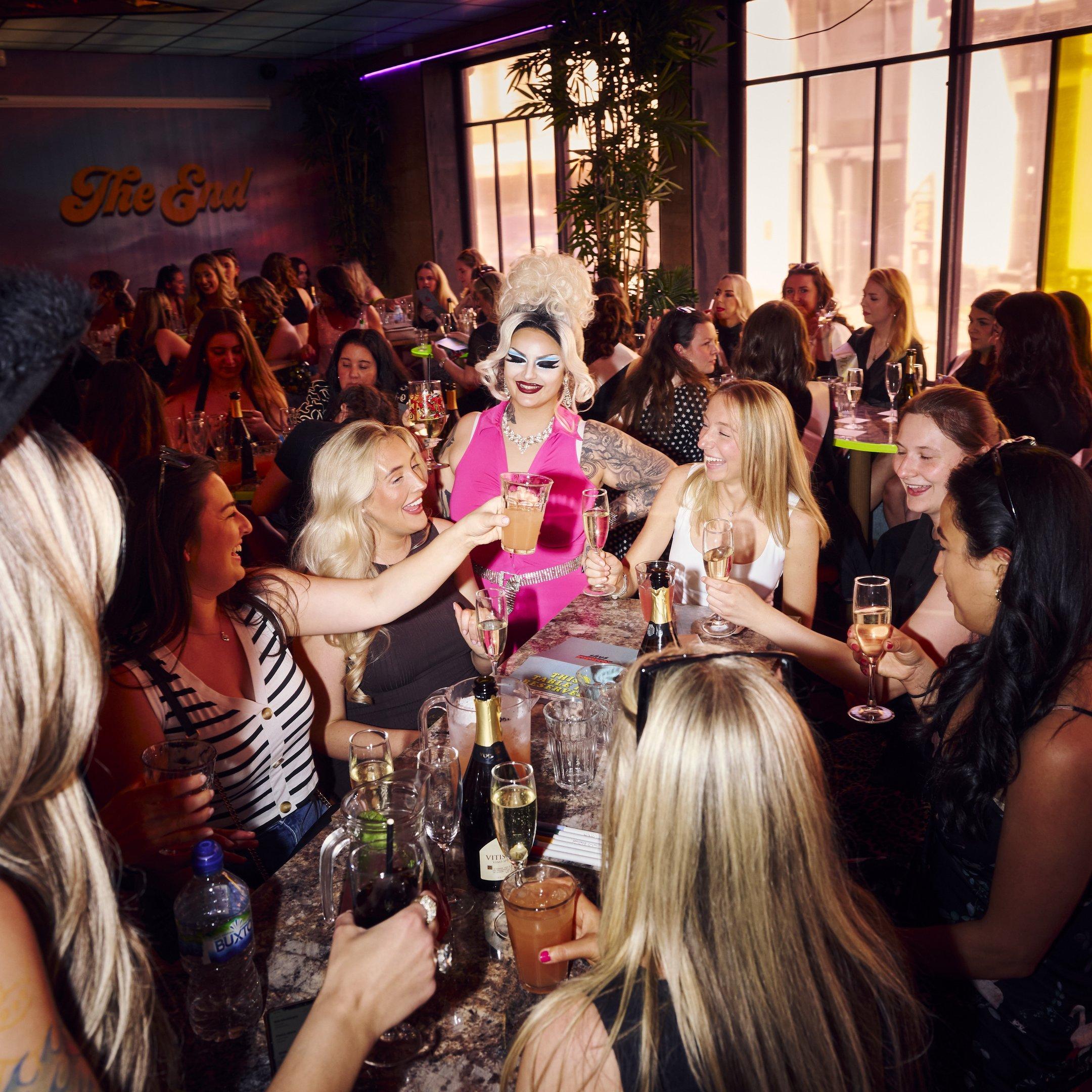 Guests sat at a table enjoying a bottomless brunch and laughing with a drag act in Nikki's bar