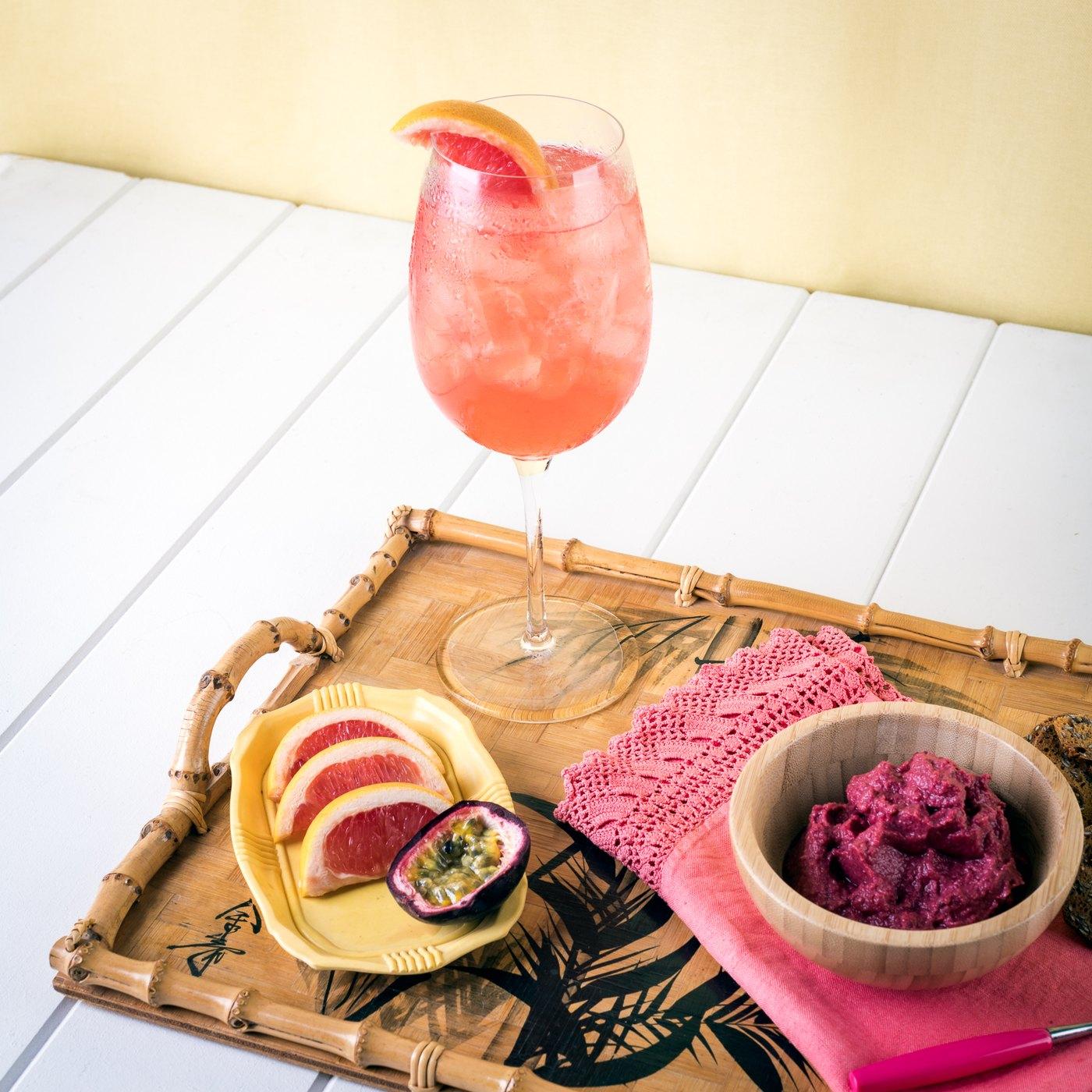 A pink Passoã cocktail on a tray beside a halved passion fruit