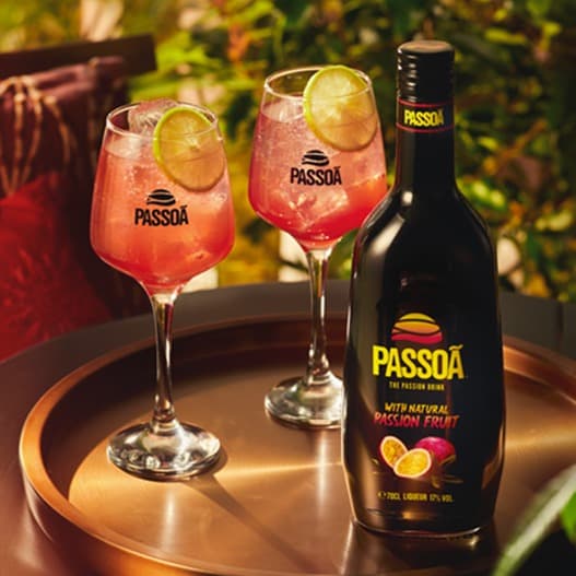 A bottle of Passoã and two pink cocktails on a copper tray in golden sunset light