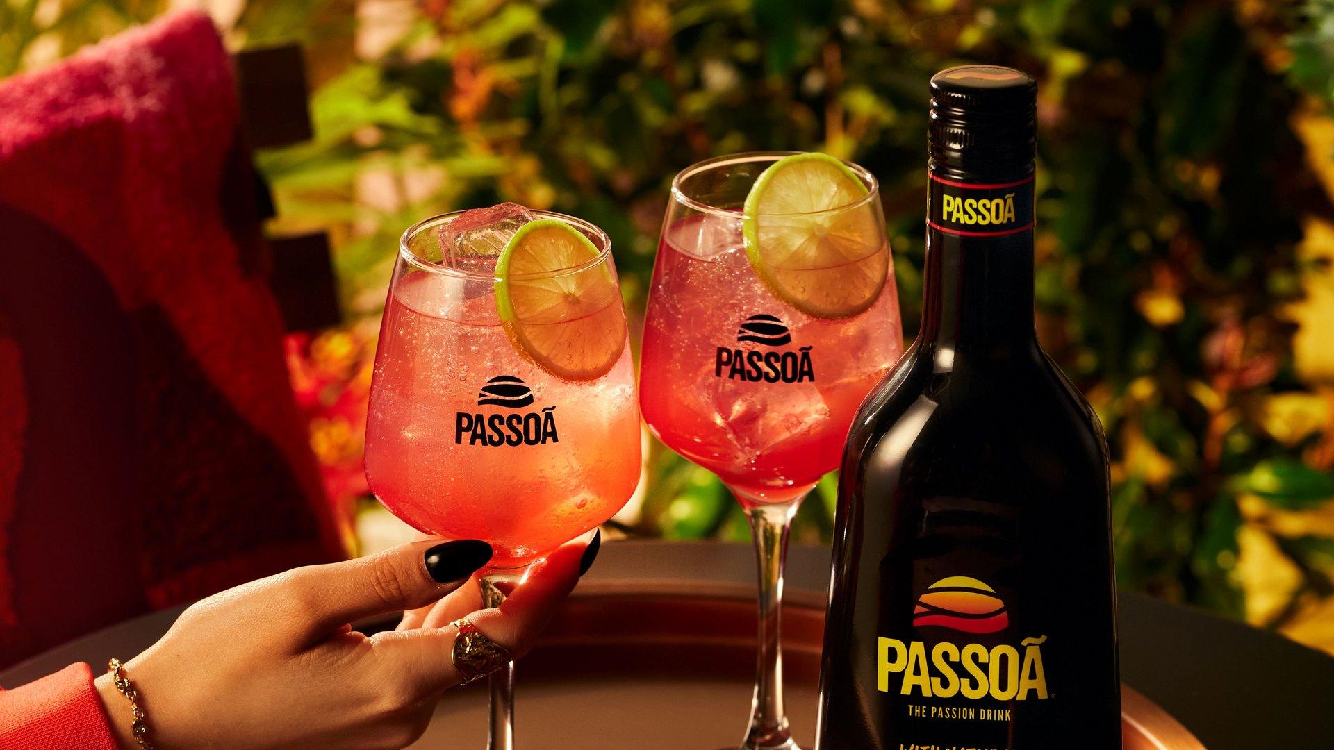 Two pink Passoã spritz cocktails with lime beside a bottle of Passoã on a copper tray