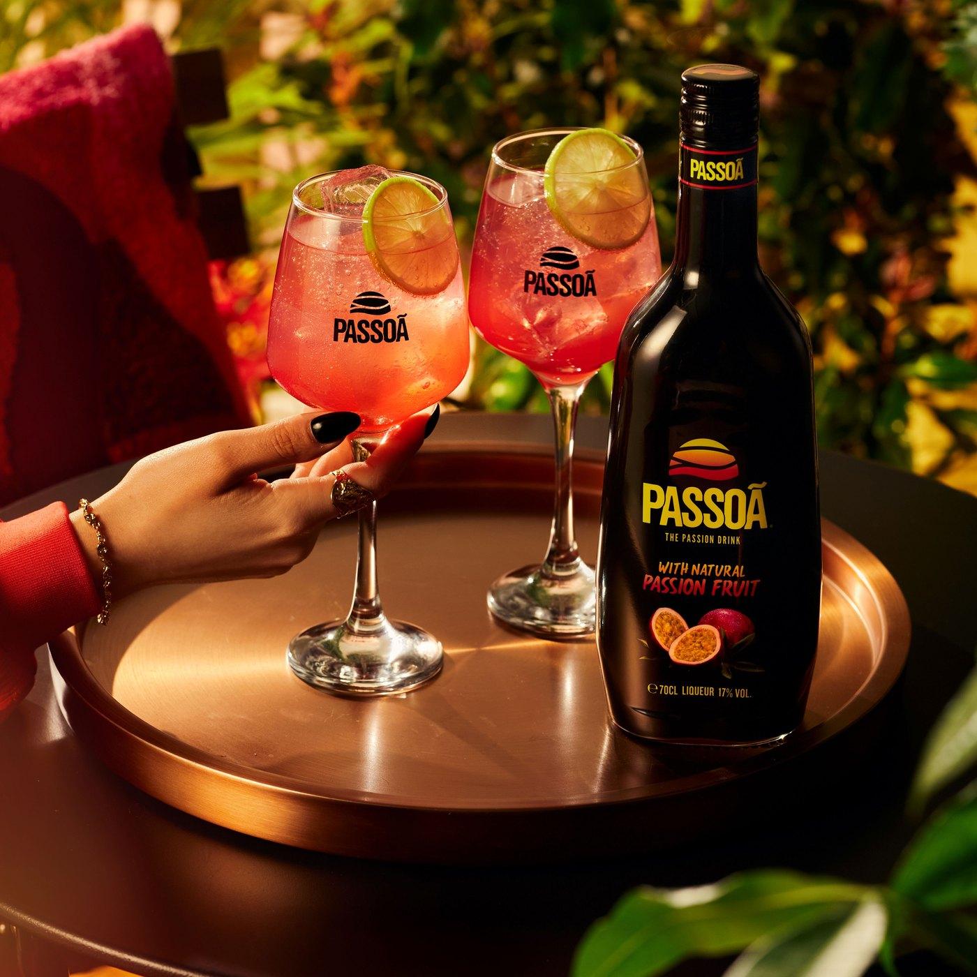 Two pink Passoã spritz cocktails with lime beside a bottle of Passoã on a copper tray