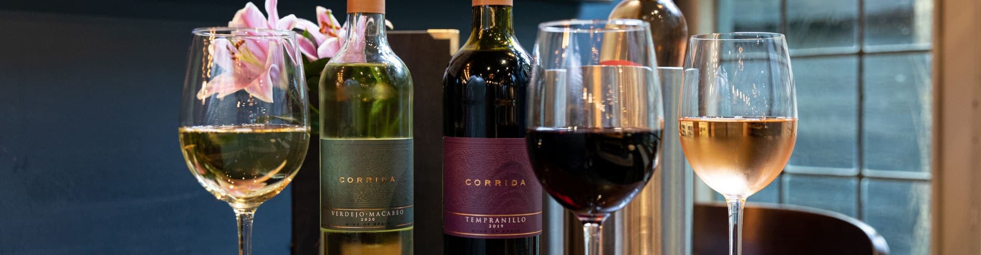 Glasses of red, white and rose wine in front of red and white wine bottles