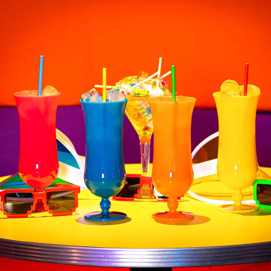 4 Popworld cocktails in bright coloured glasses lined up on a table