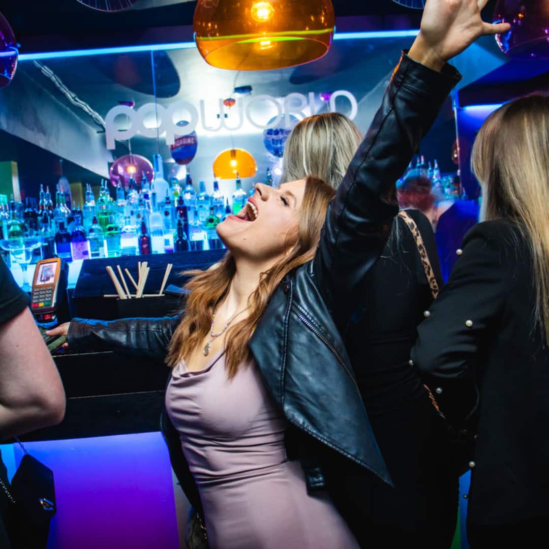 Popworld guest singing with their hand in the air at the bar