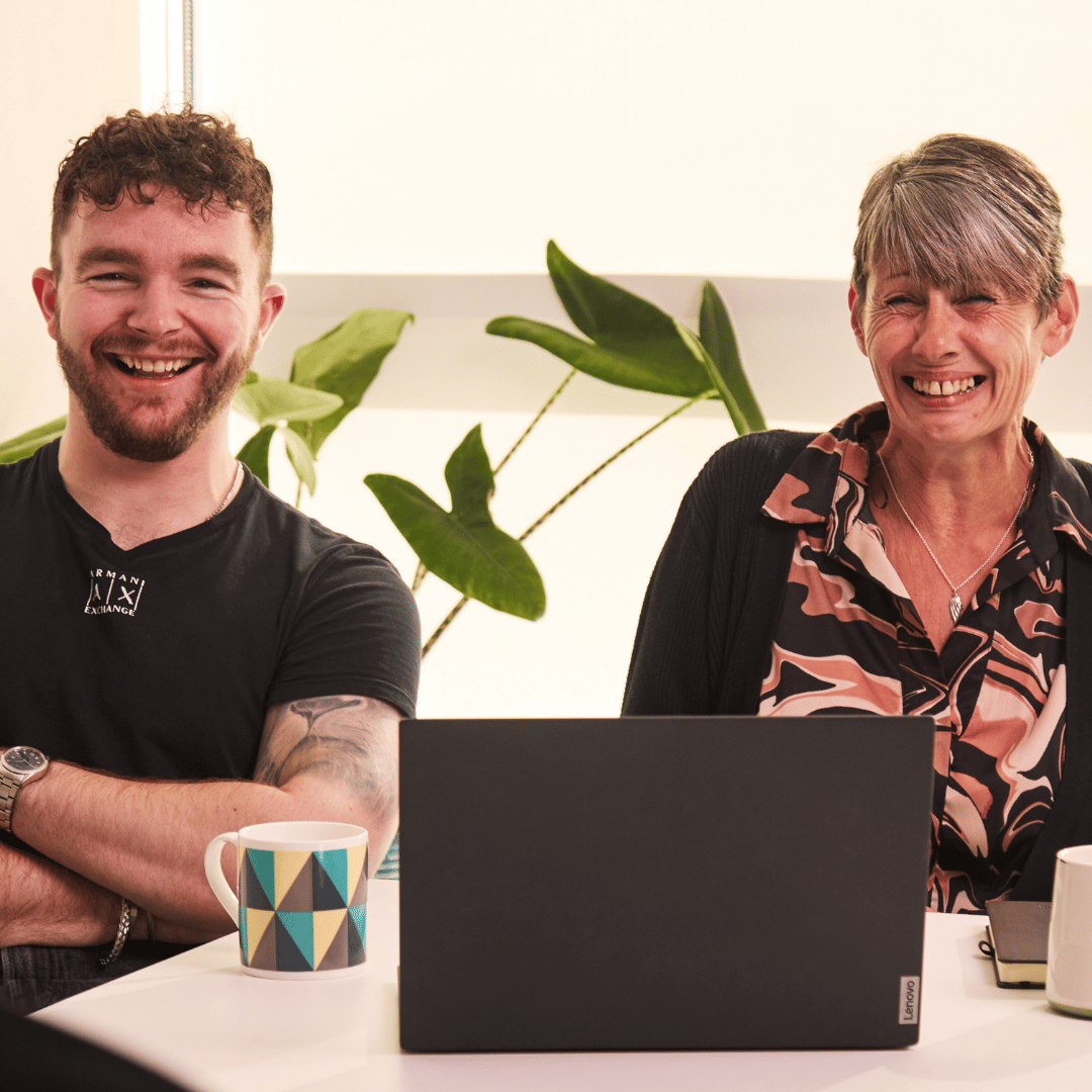 Two Finance team members smiling with a laptop in front.