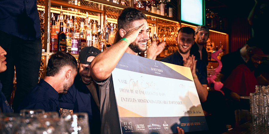 Jan holding a cheque behind the bar for winning Most Knowledgeable Bartender
