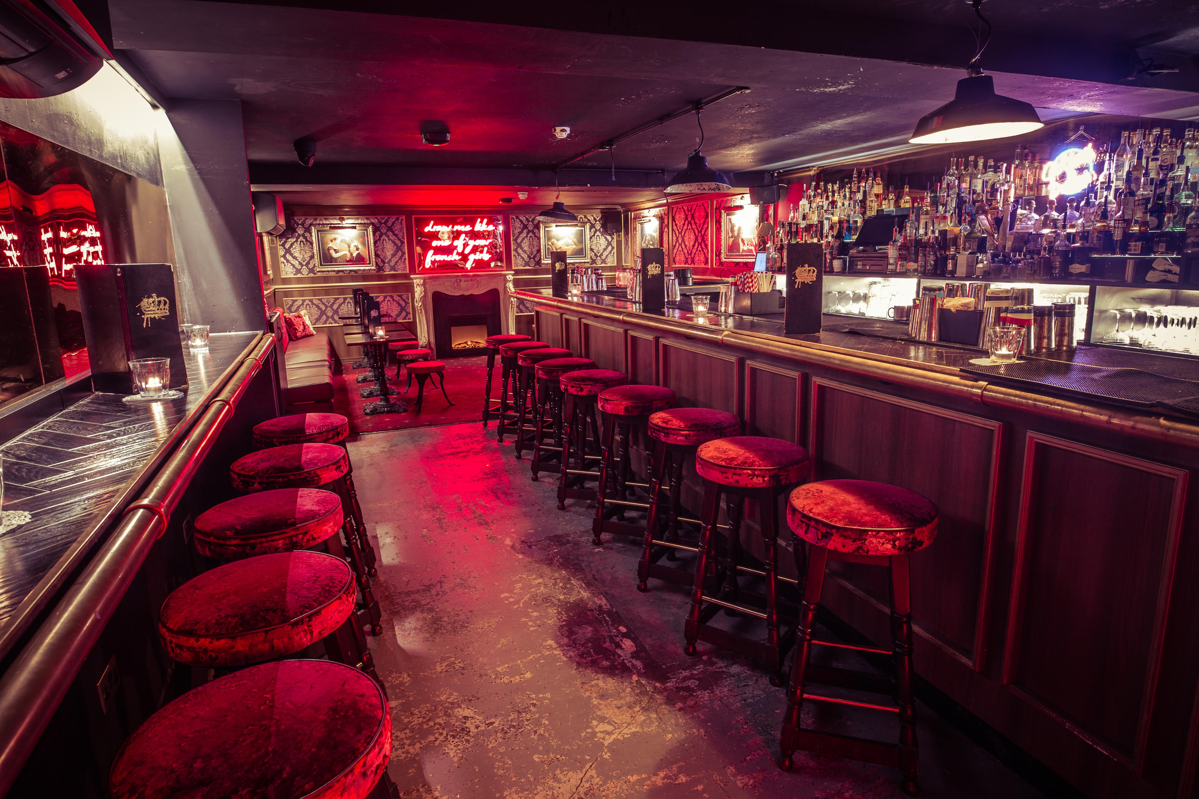 A bar area with red velvet stools and a red neon sign