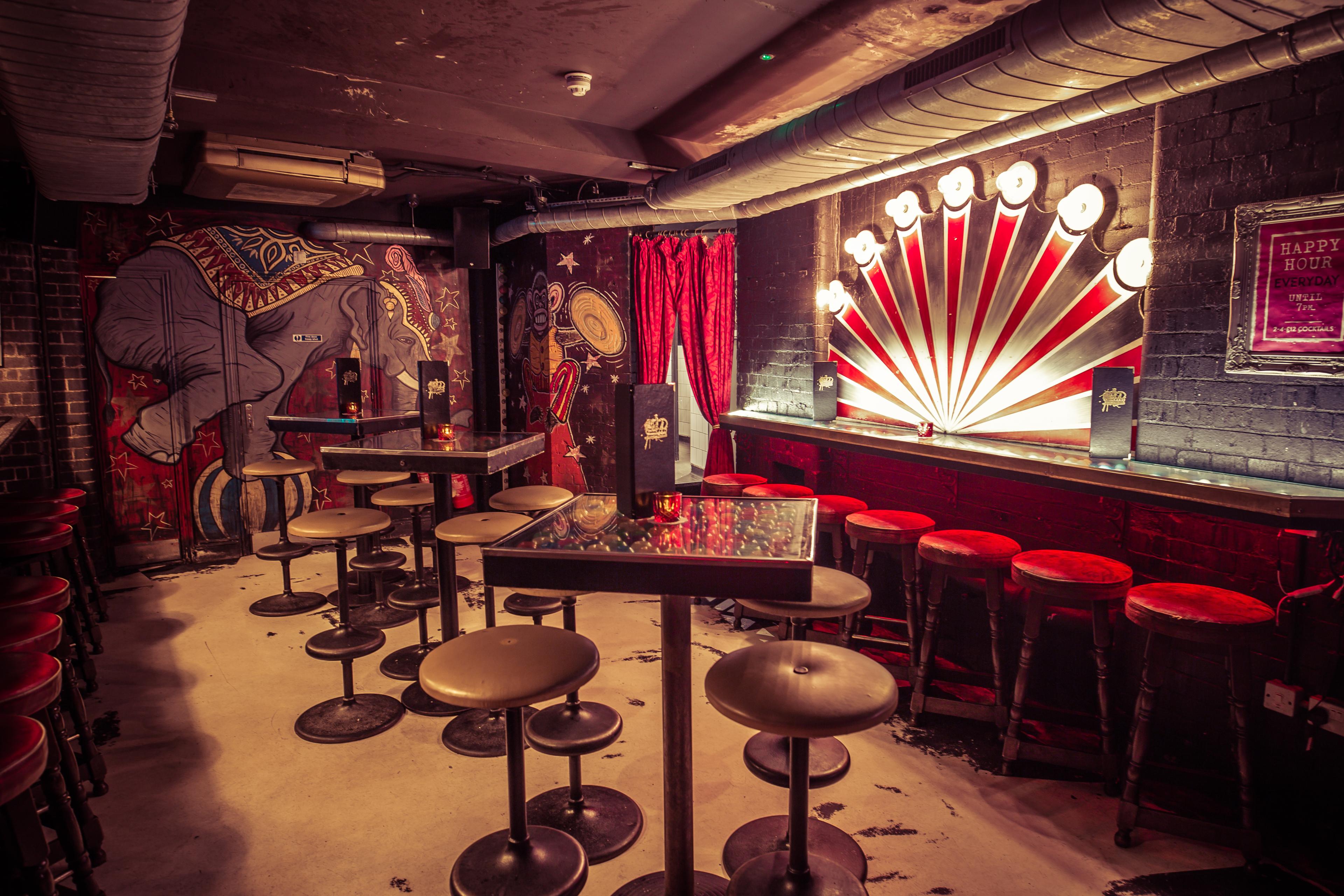 A circus themed bar area with wall art and high tables and stool seating